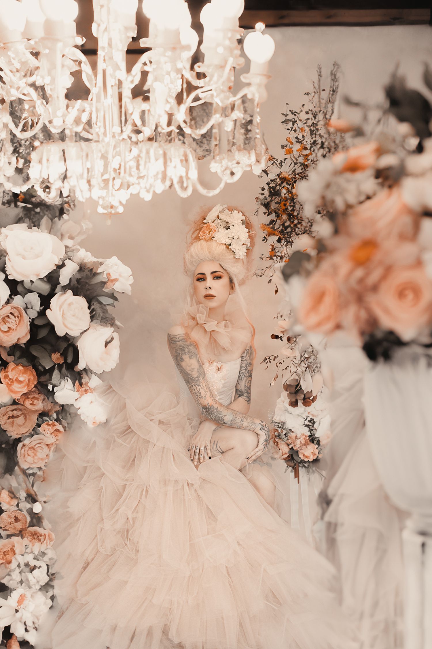 Romantic scene with crystal chandeliers, peach roses, and soft white tulle in an elegant setting.