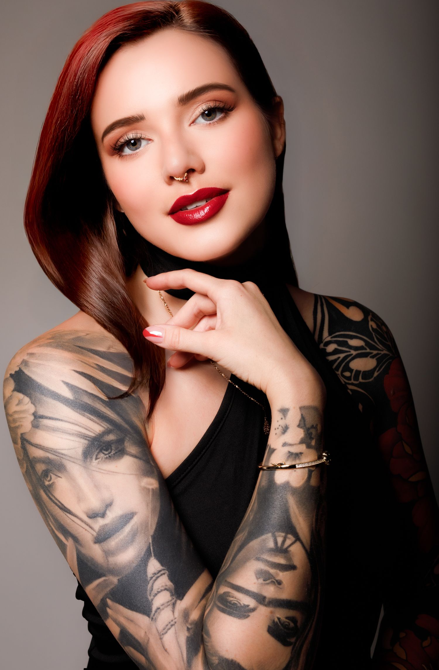 Studio portrait of a model with red lipstick and sleeve tattoos against a dark background.