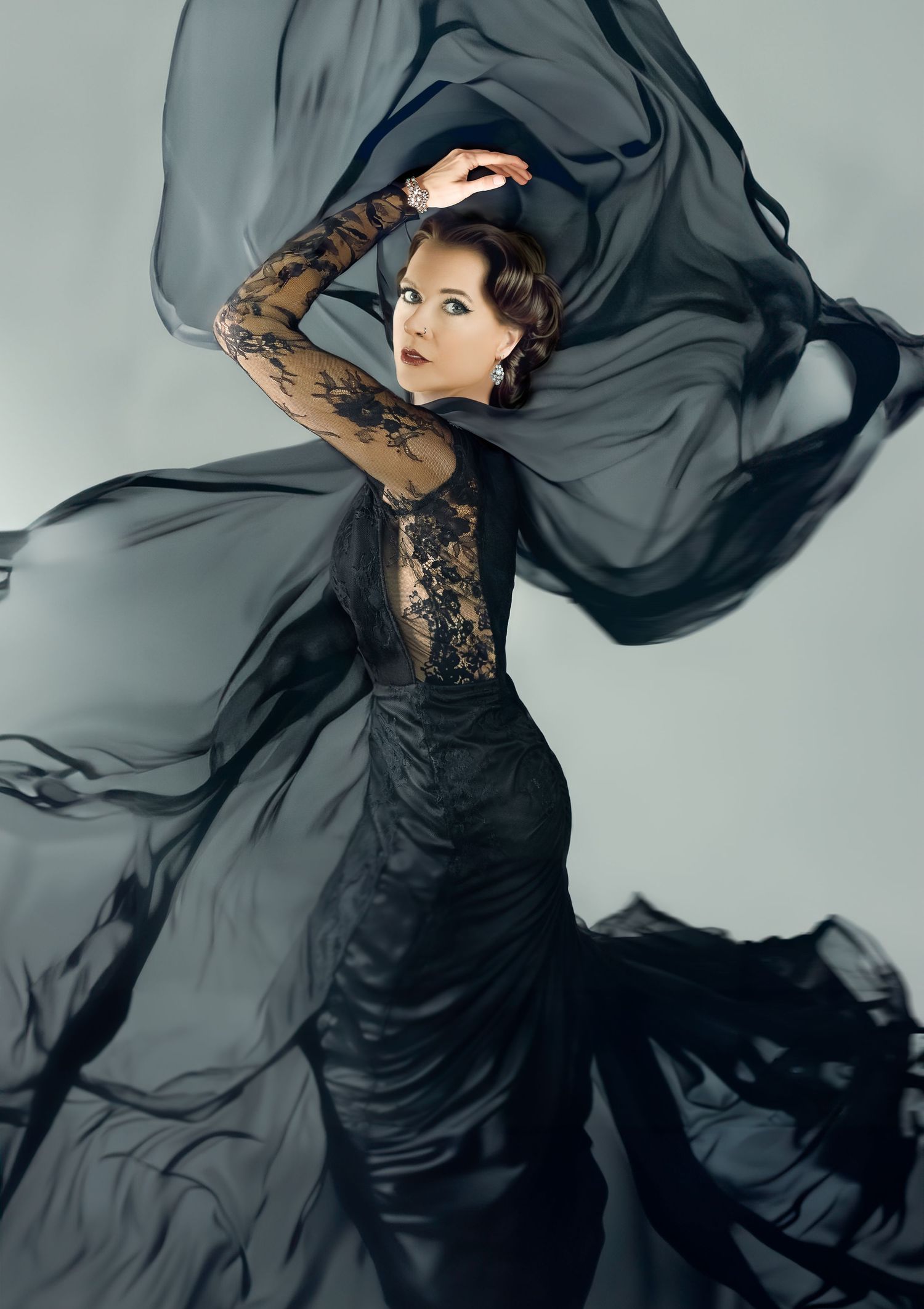 Fashion model in black lace dress with flowing gray fabric creating dynamic movement.