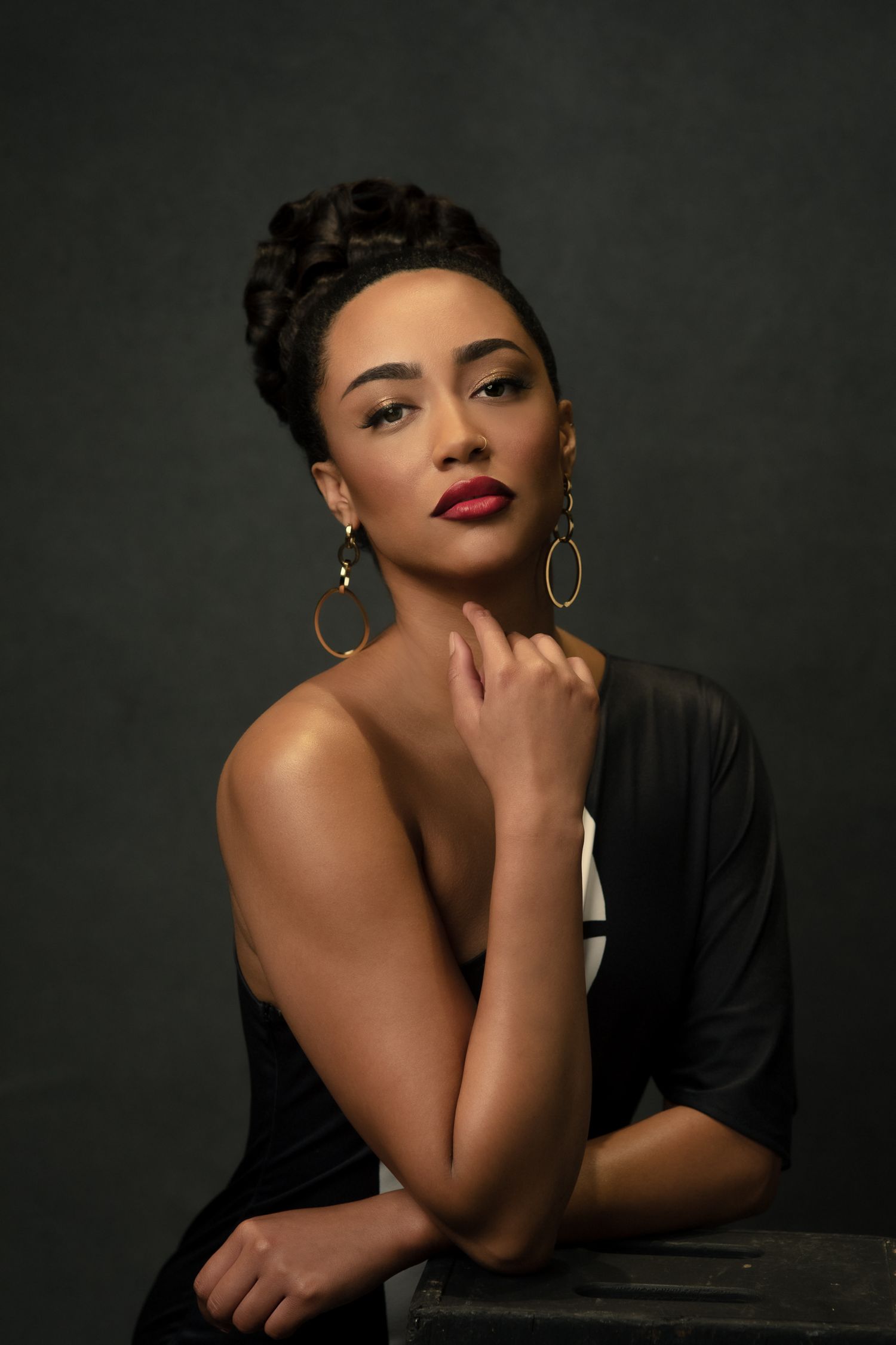 Glamour portrait in dramatic lighting featuring elegant poses and hoop earrings against dark background.