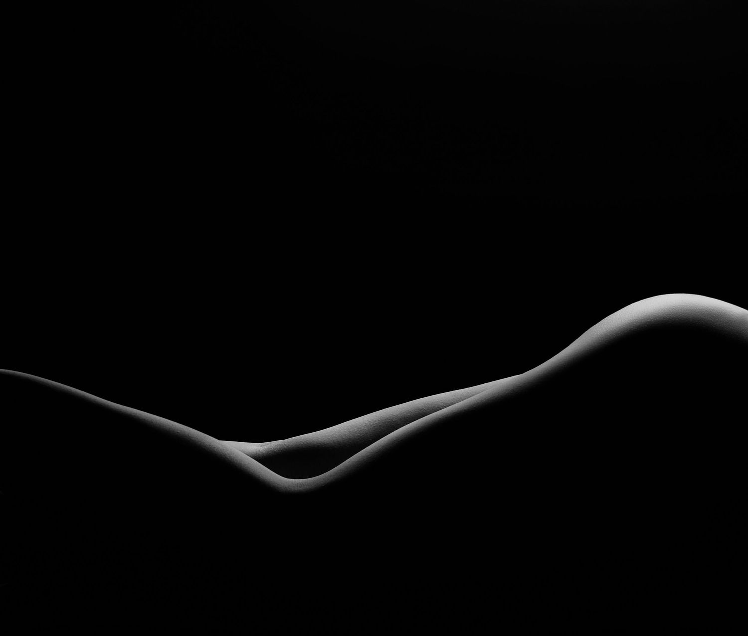 Black and white fine art nude photography showcasing abstract body curves against a dark background.