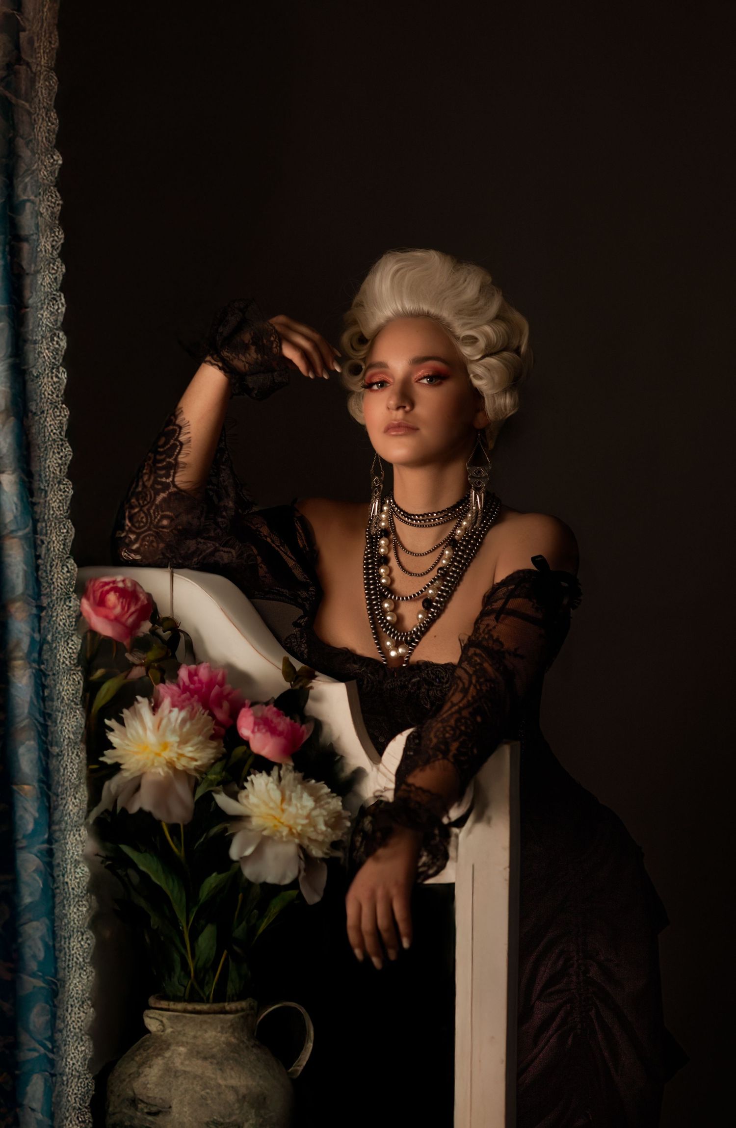 Vintage-inspired photoshoot with lace details, statement jewelry, and flowers in moody lighting.