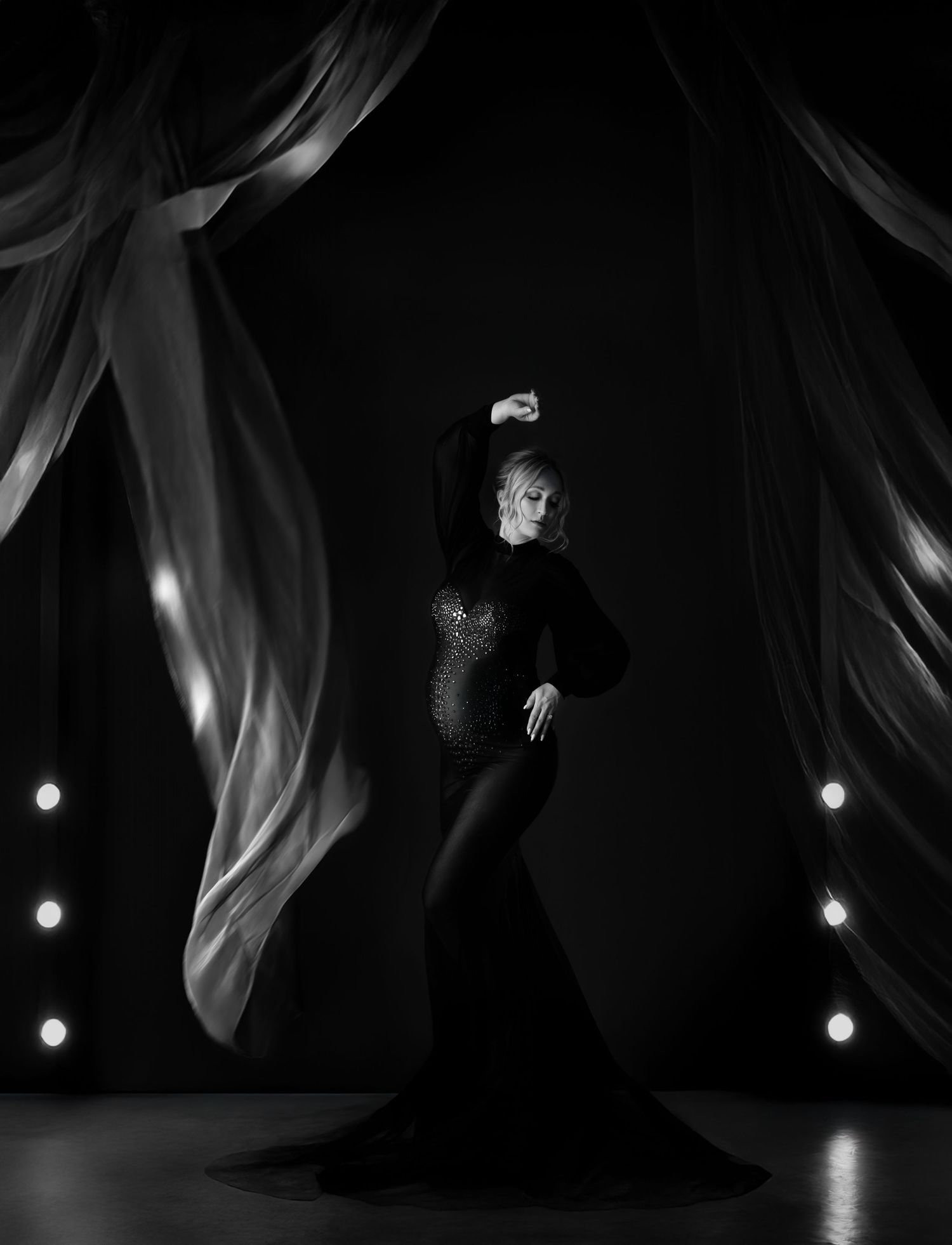 Dramatic silhouette of flowing gown and fabric movement captured against dark background with spotlights.
