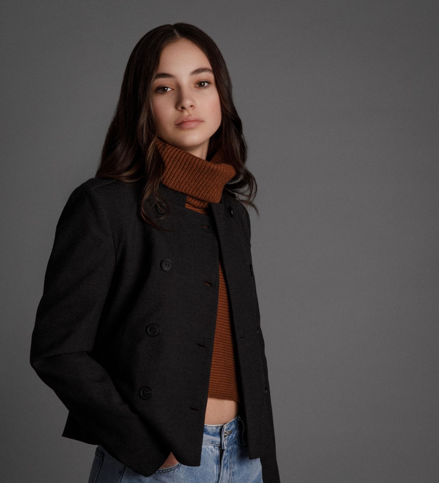 Fashion portrait featuring black jacket and brown turtleneck against grey studio background.