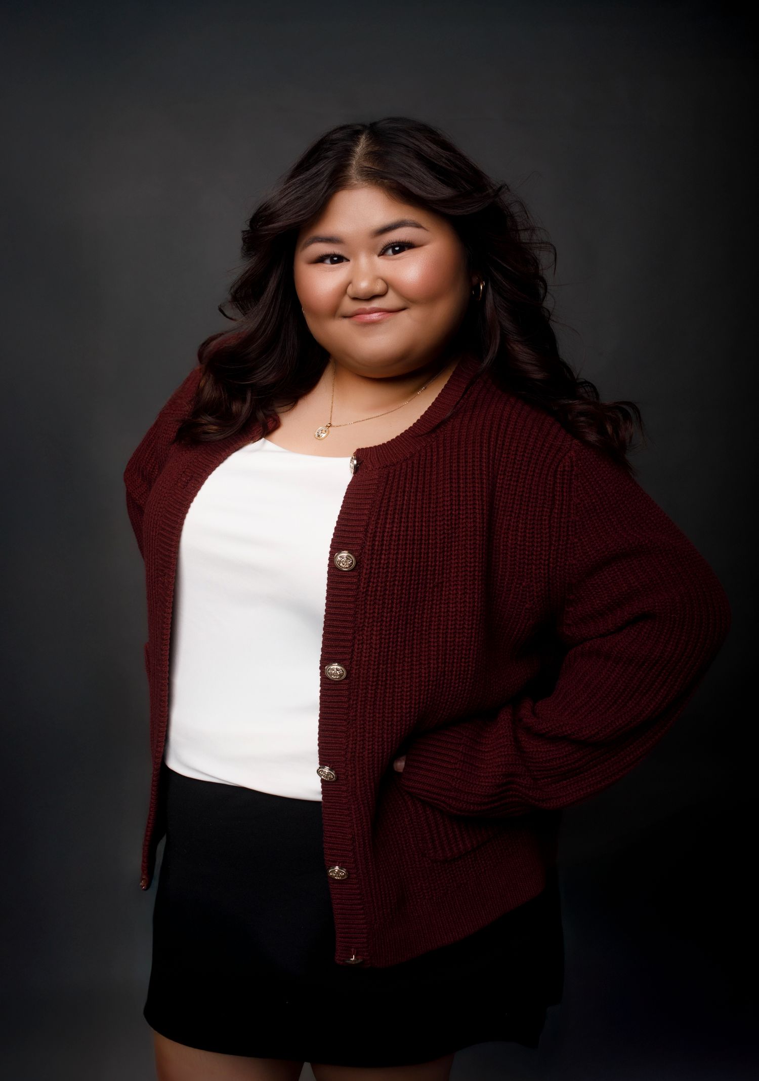 Portrait photography session showing fashionable burgundy cardigan and white top against dark background.