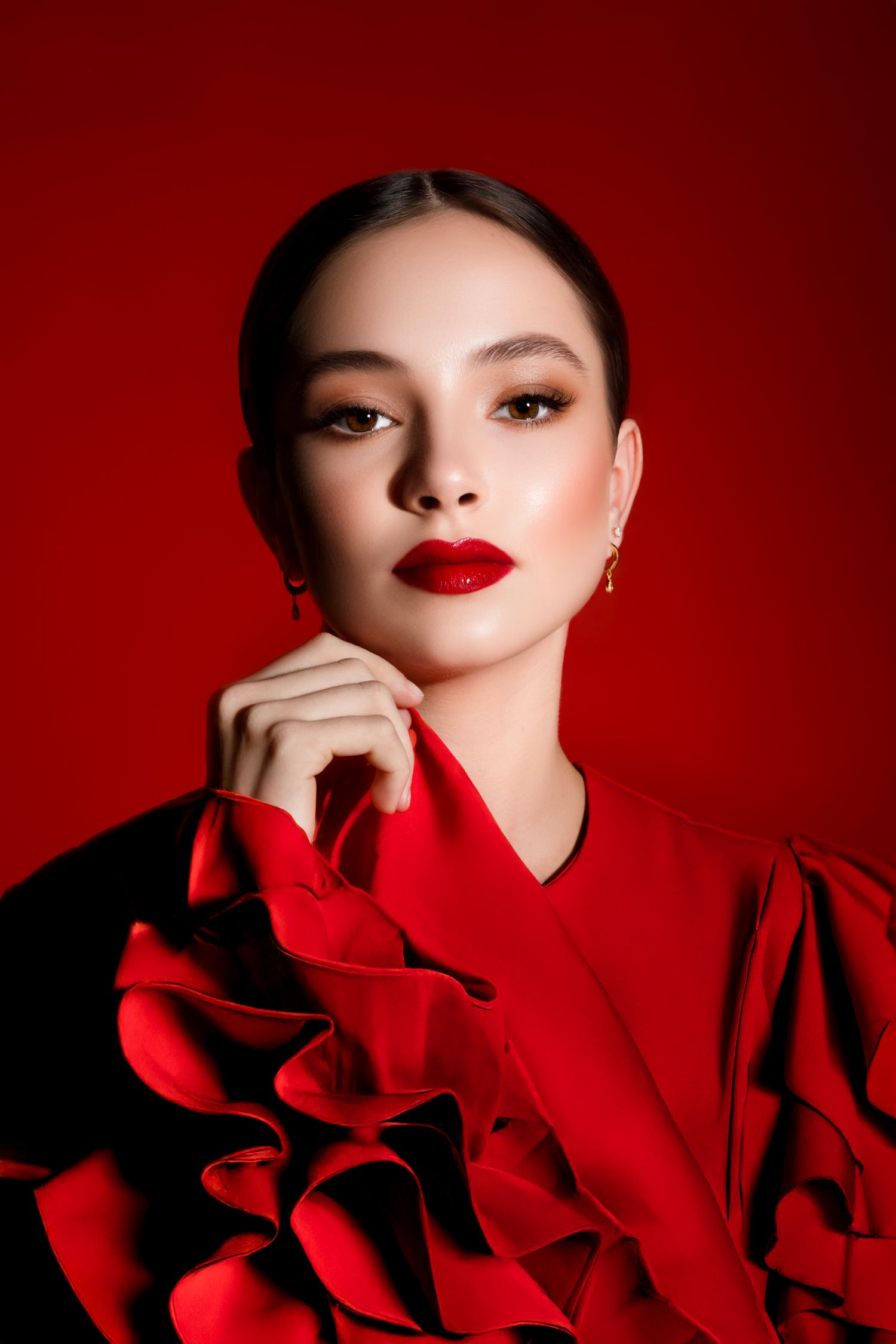 Dramatic fashion portraits against red background featuring bold makeup and ruffled clothing.