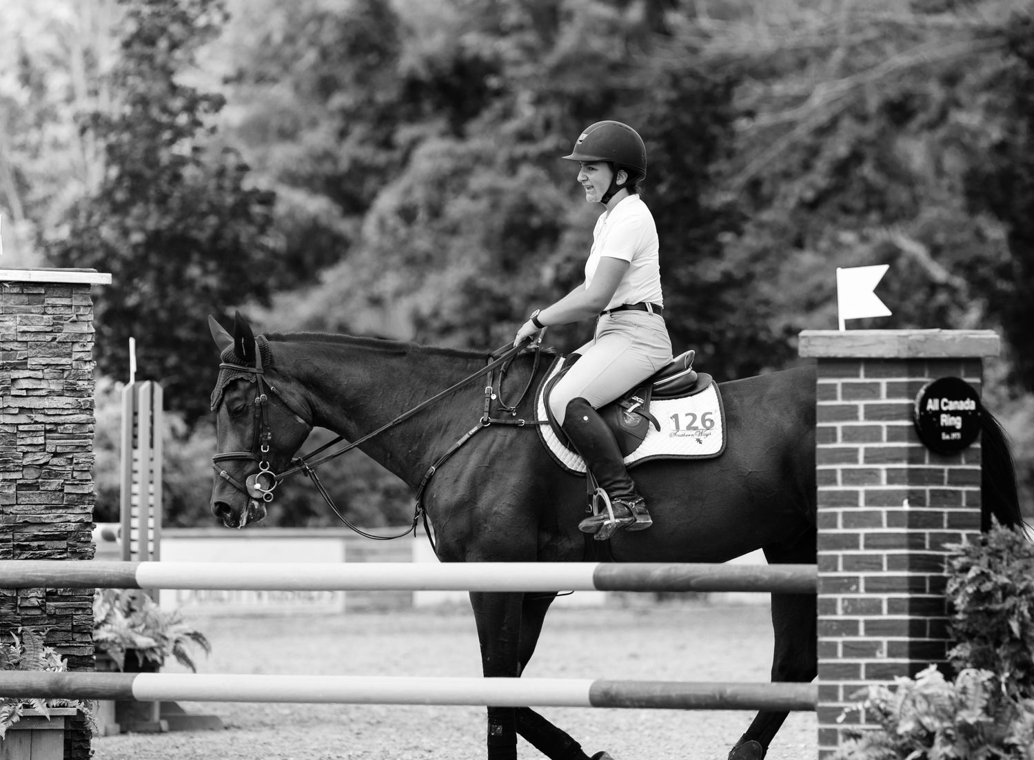 Black and white photograph of horse and rider jumping over competition fence.