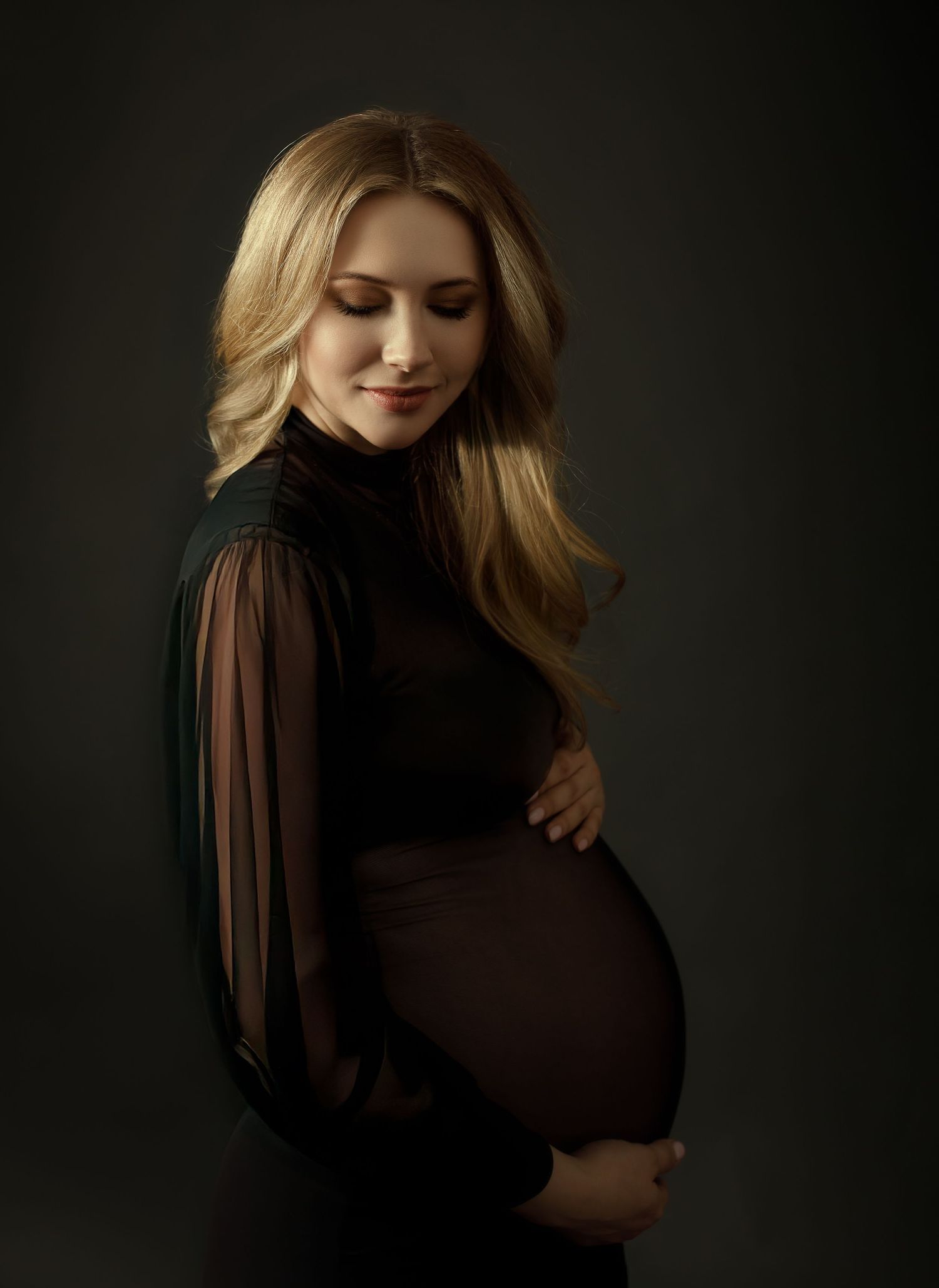 Dramatic maternity portraits in a brown dress against dark background showing pregnancy silhouette.