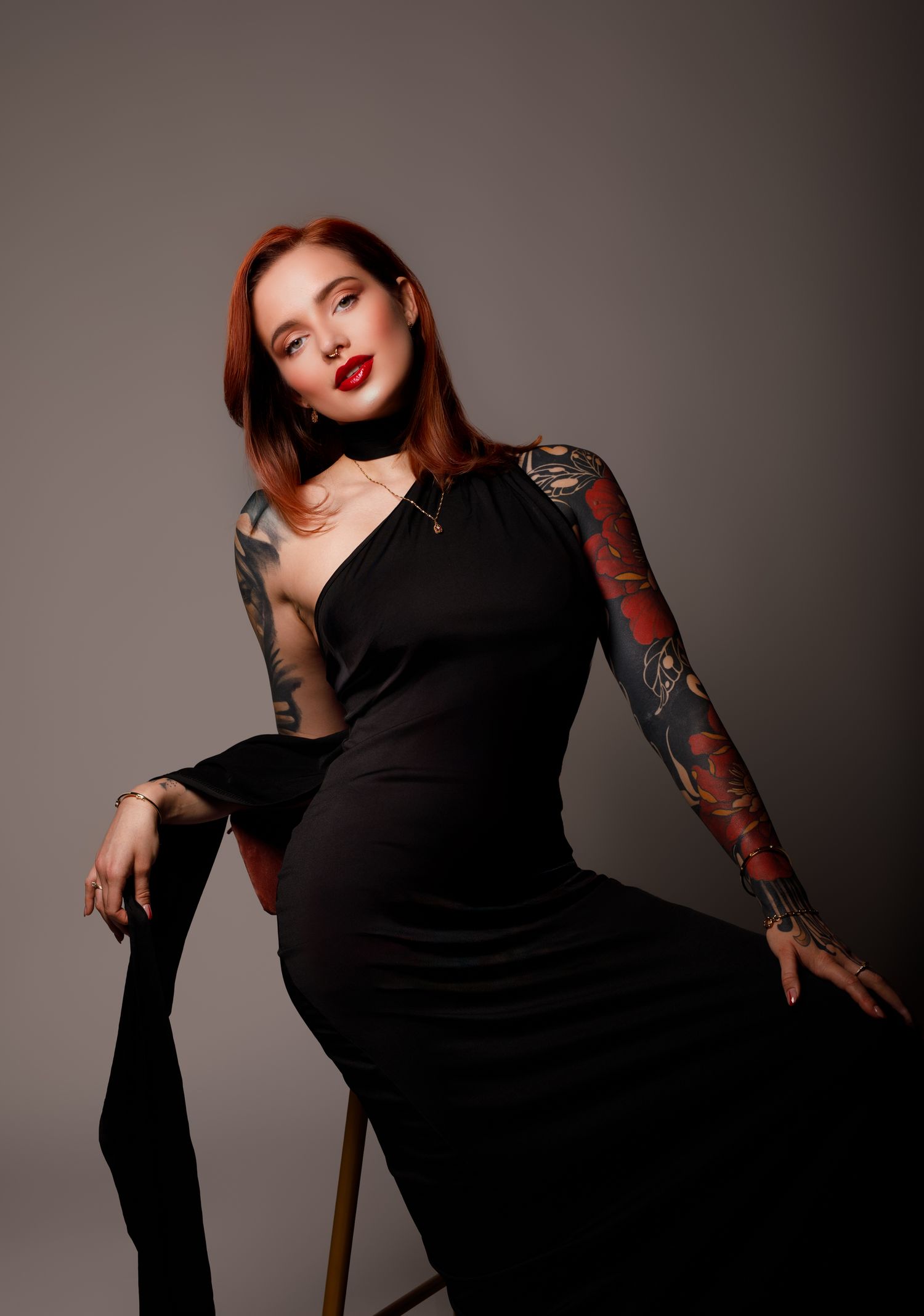 Fashion model in black dress poses dramatically with tattoo sleeve in studio setting.