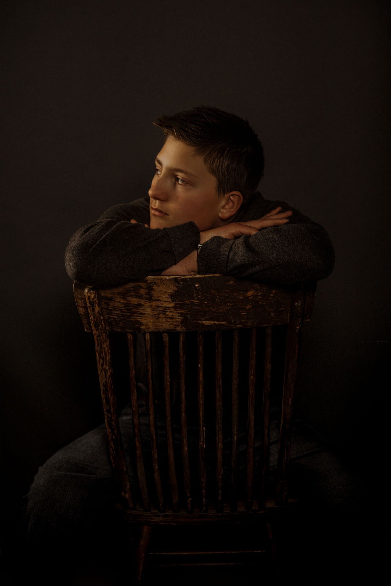 A series of dark moody portraits showing someone seated in a vintage wooden chair against a black background.