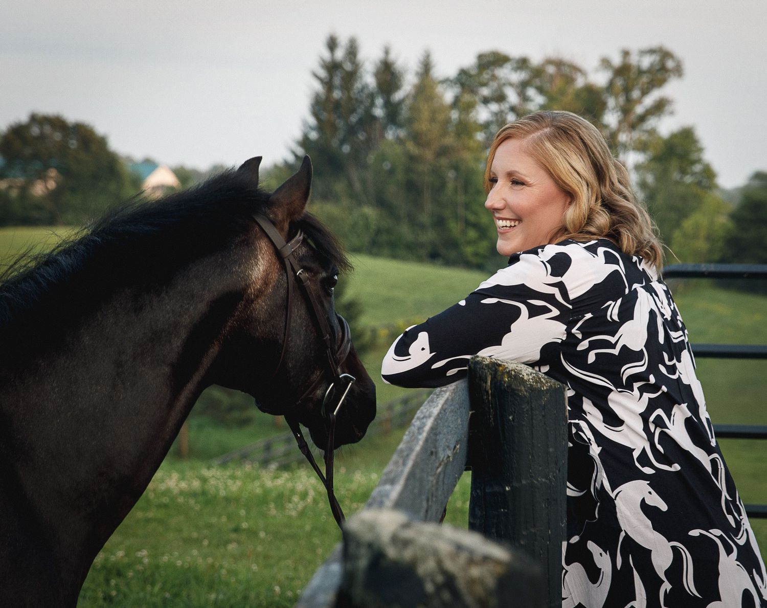 A horse and rider share a tender moment in a field wearing a black and white patterned jacket.