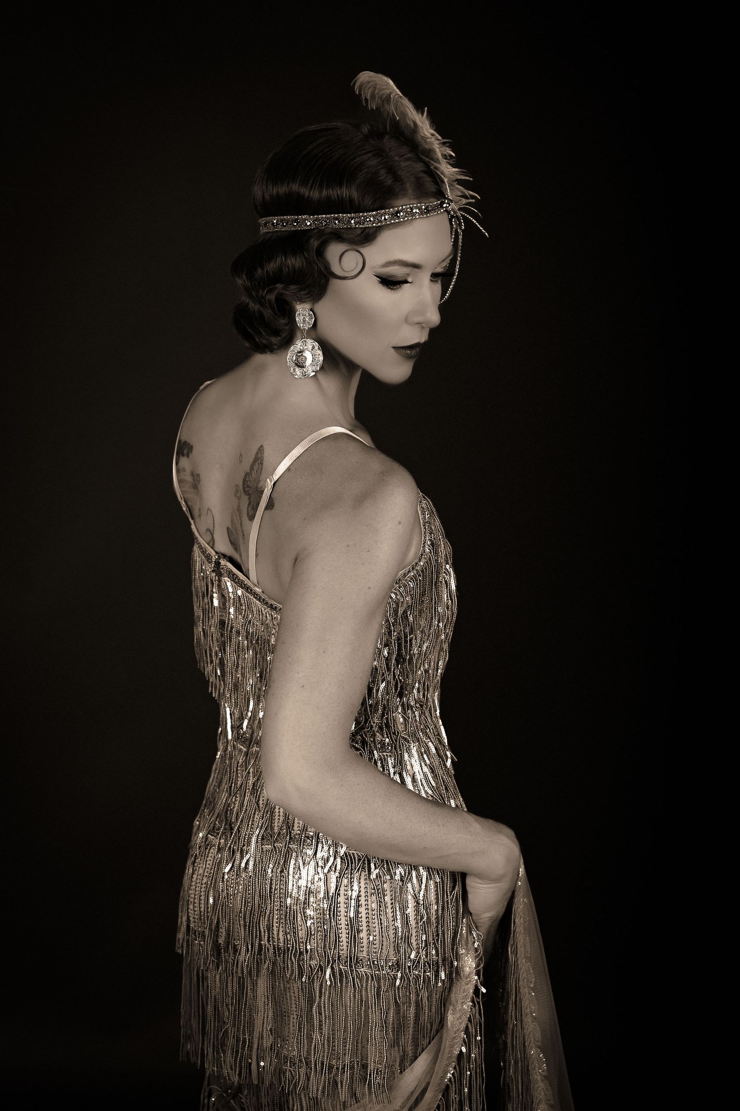 Vintage-style portrait in 1920s flapper dress with feather headpiece and fringe details.