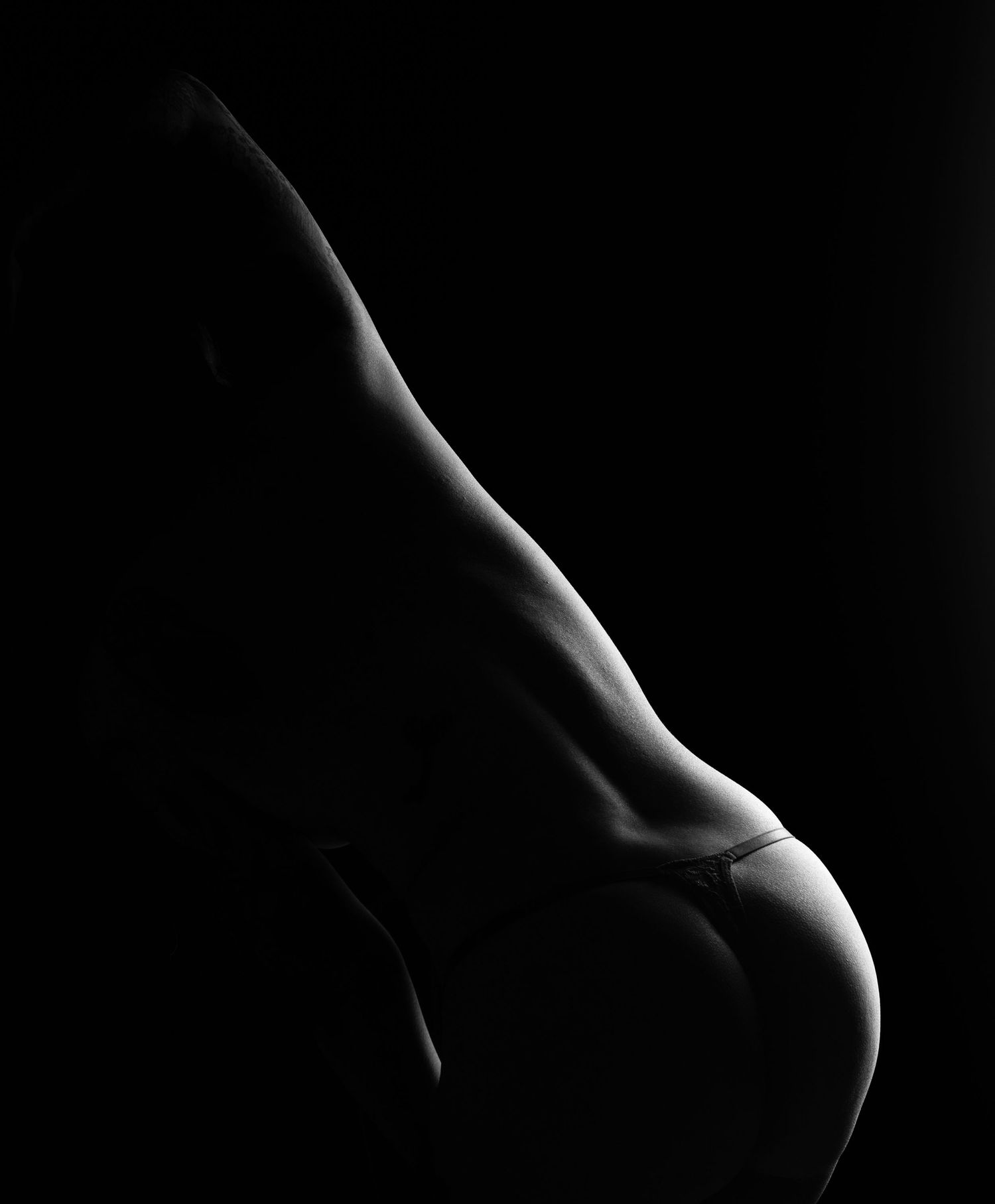 Black and white artistic silhouette photograph highlighting the curves of a human form against a dark background.