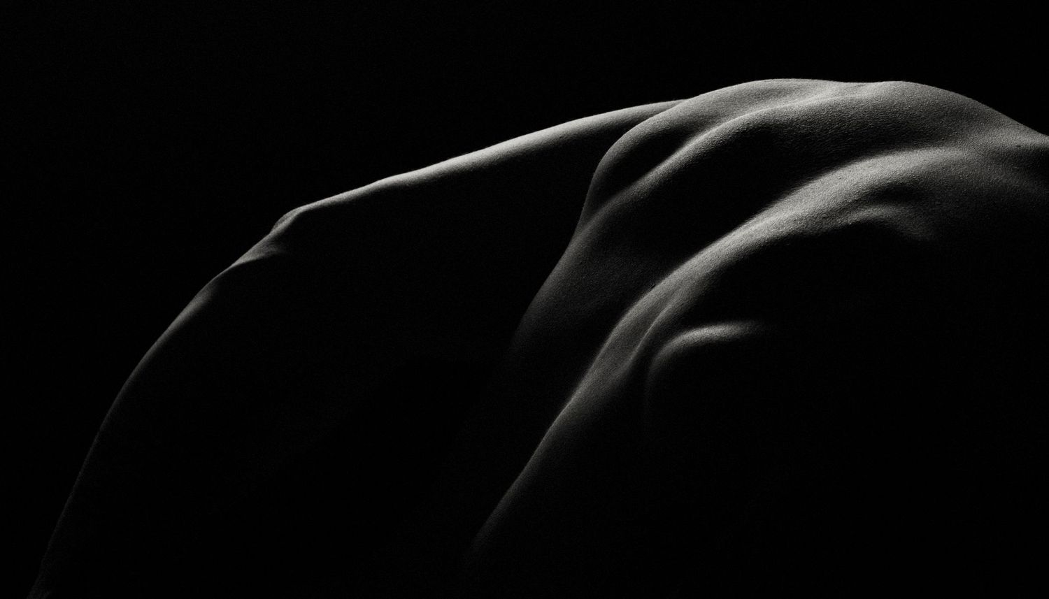 Black and white artistic photograph highlighting the curves and contours of a human body against a dark background.