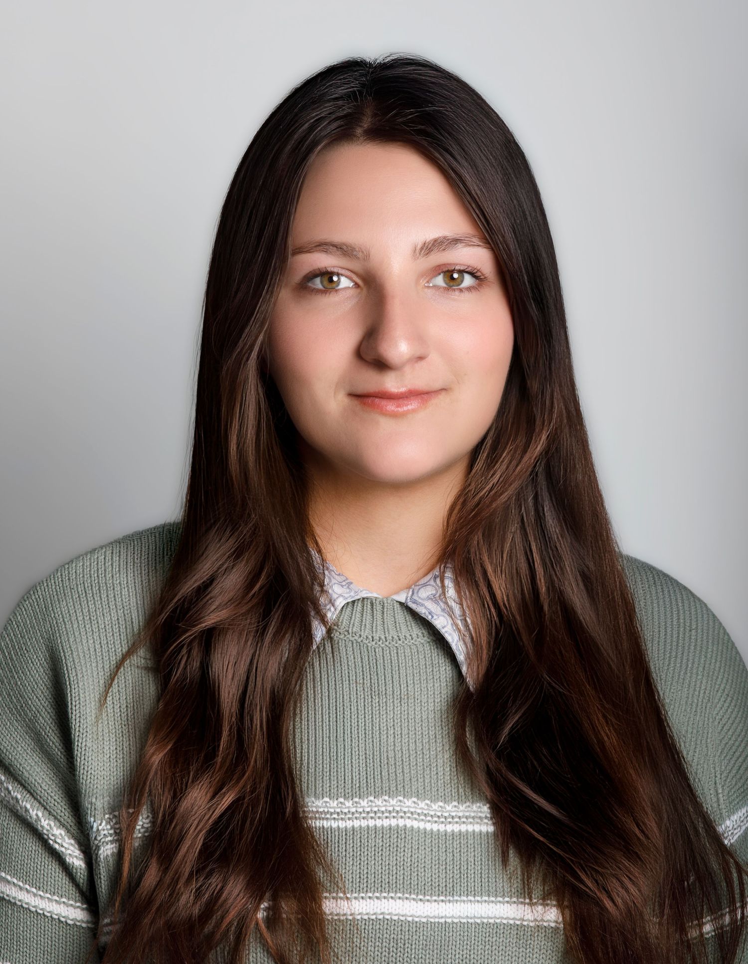Young woman with long dark hair and green eyes wearing a sage green ribbed sweater against a gray background.