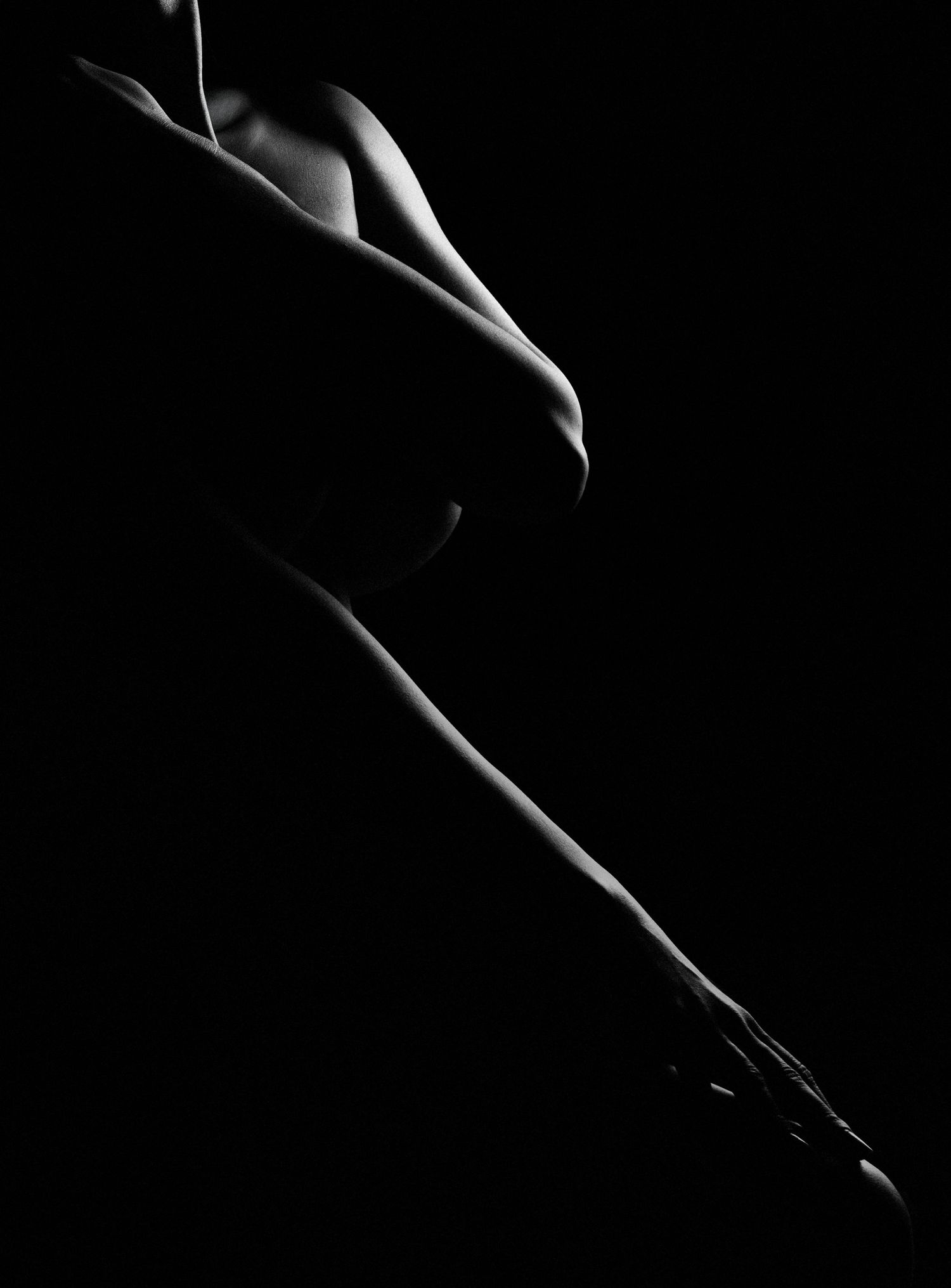 Artistic black and white fine art nude silhouette with dramatic low-key lighting highlighting body curves.