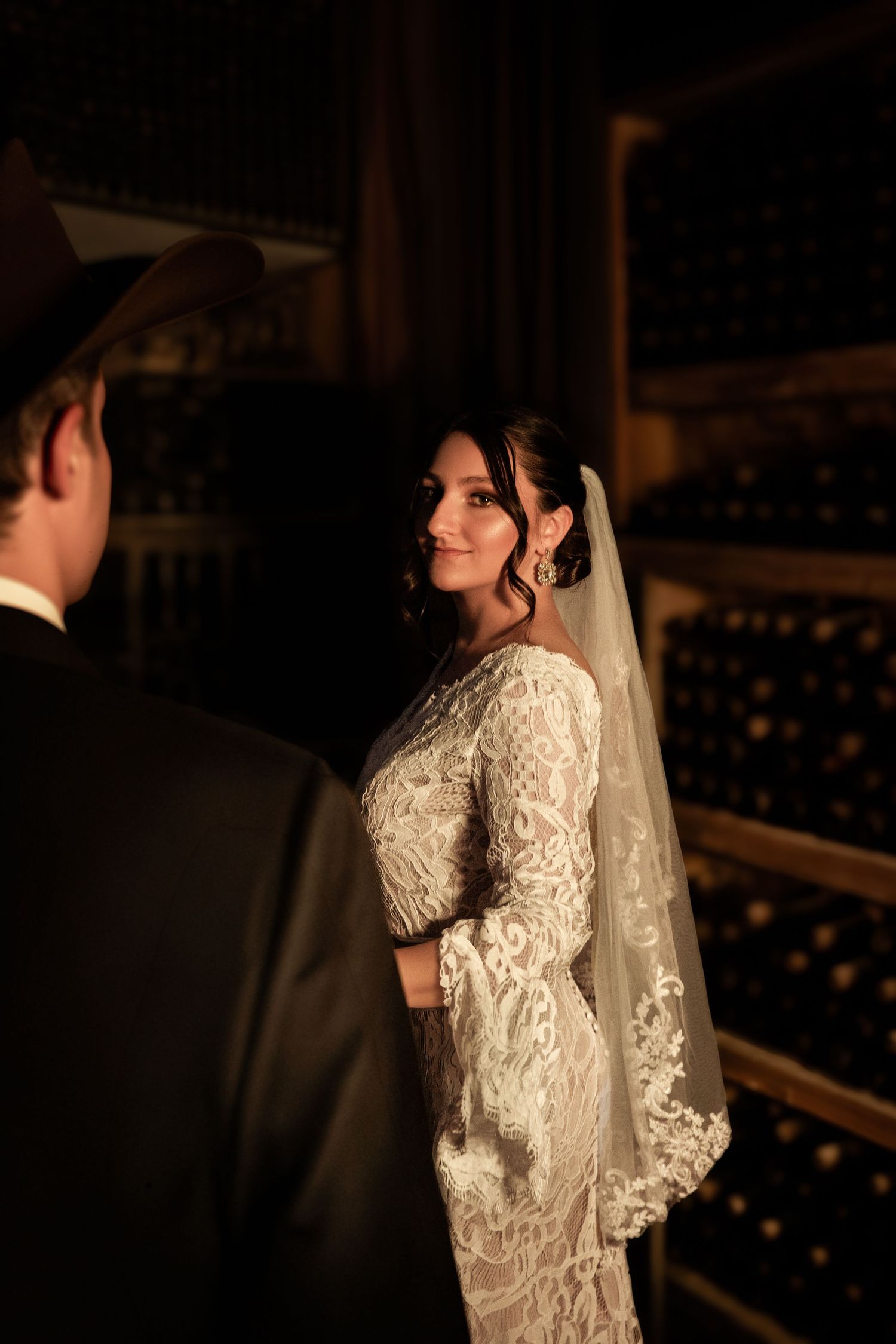 A bride in a vintage-inspired lace wedding dress with puff sleeves stands in a dimly lit venue.