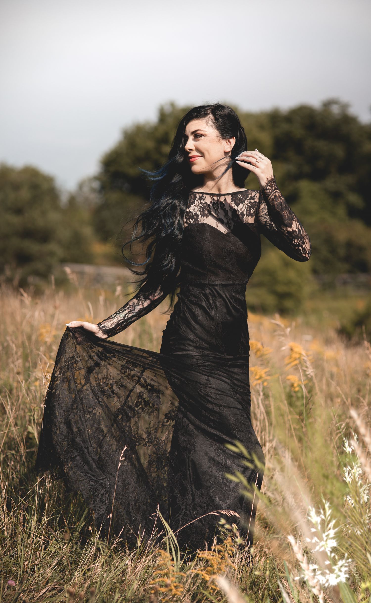 Elopement in a black lace dress twirls gracefully in a sunlit meadow.