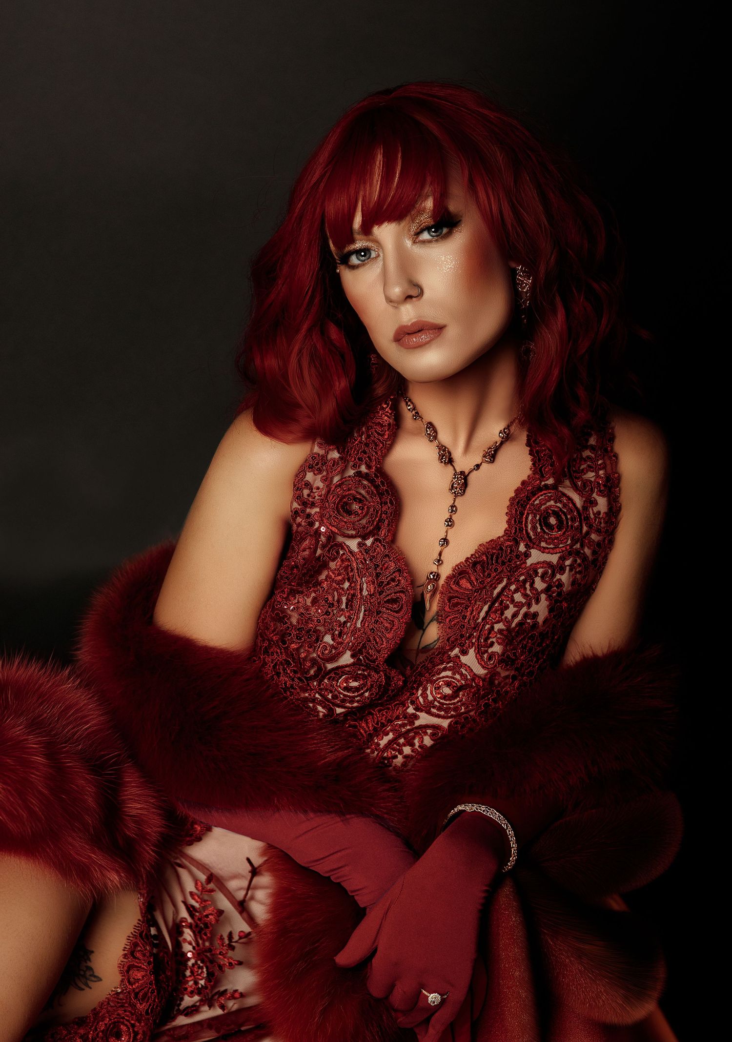 Dramatic fashion photography in deep red tones featuring luxurious gown and jewelry styling.