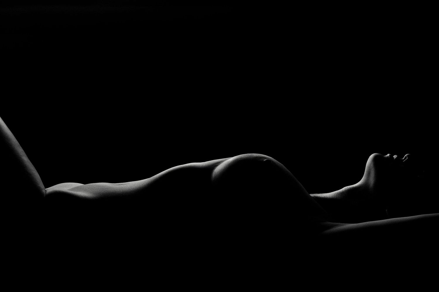Artistic black and white nude silhouette of a reclining figure with dramatic low-key lighting highlighting body curves.