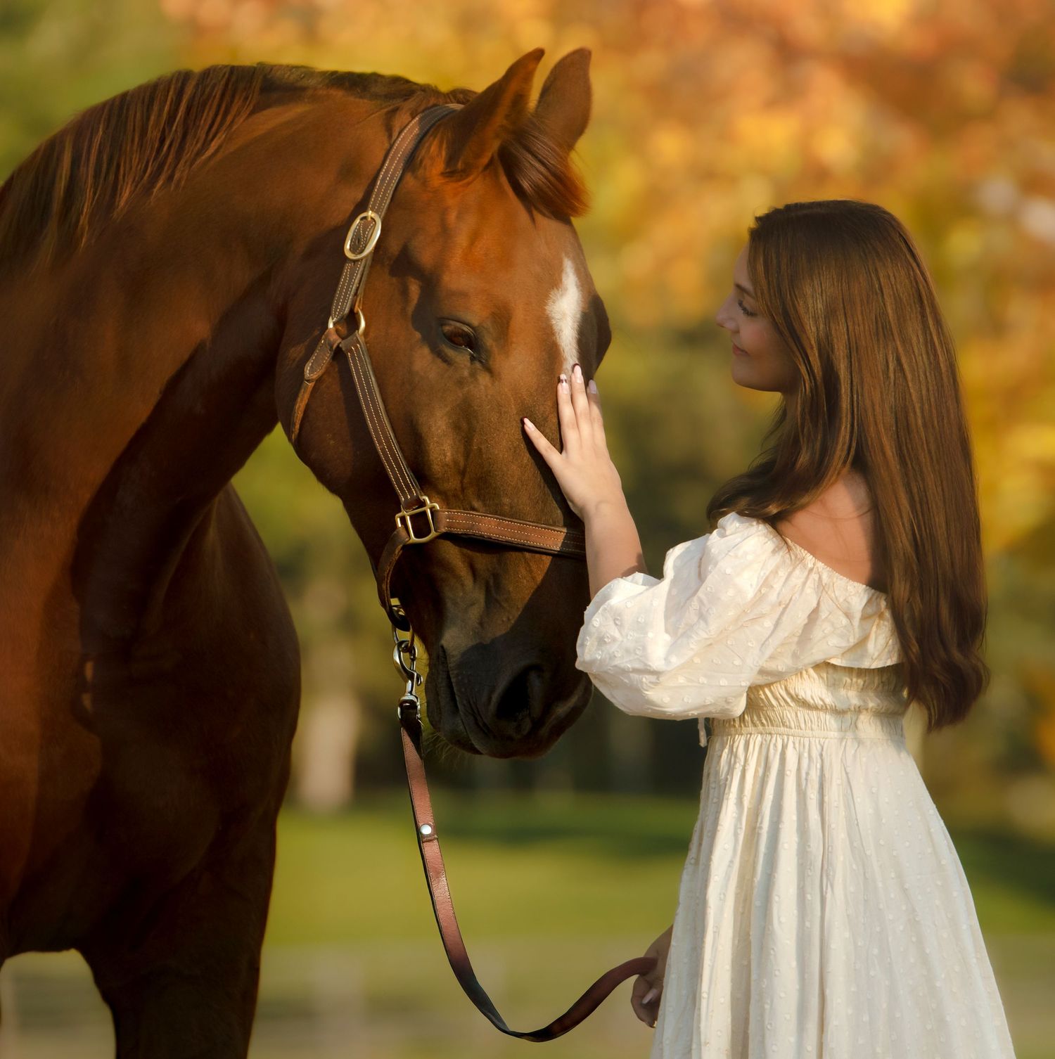 A chestnut horse and rider in vintage white dress share a moment in autumn scenery.