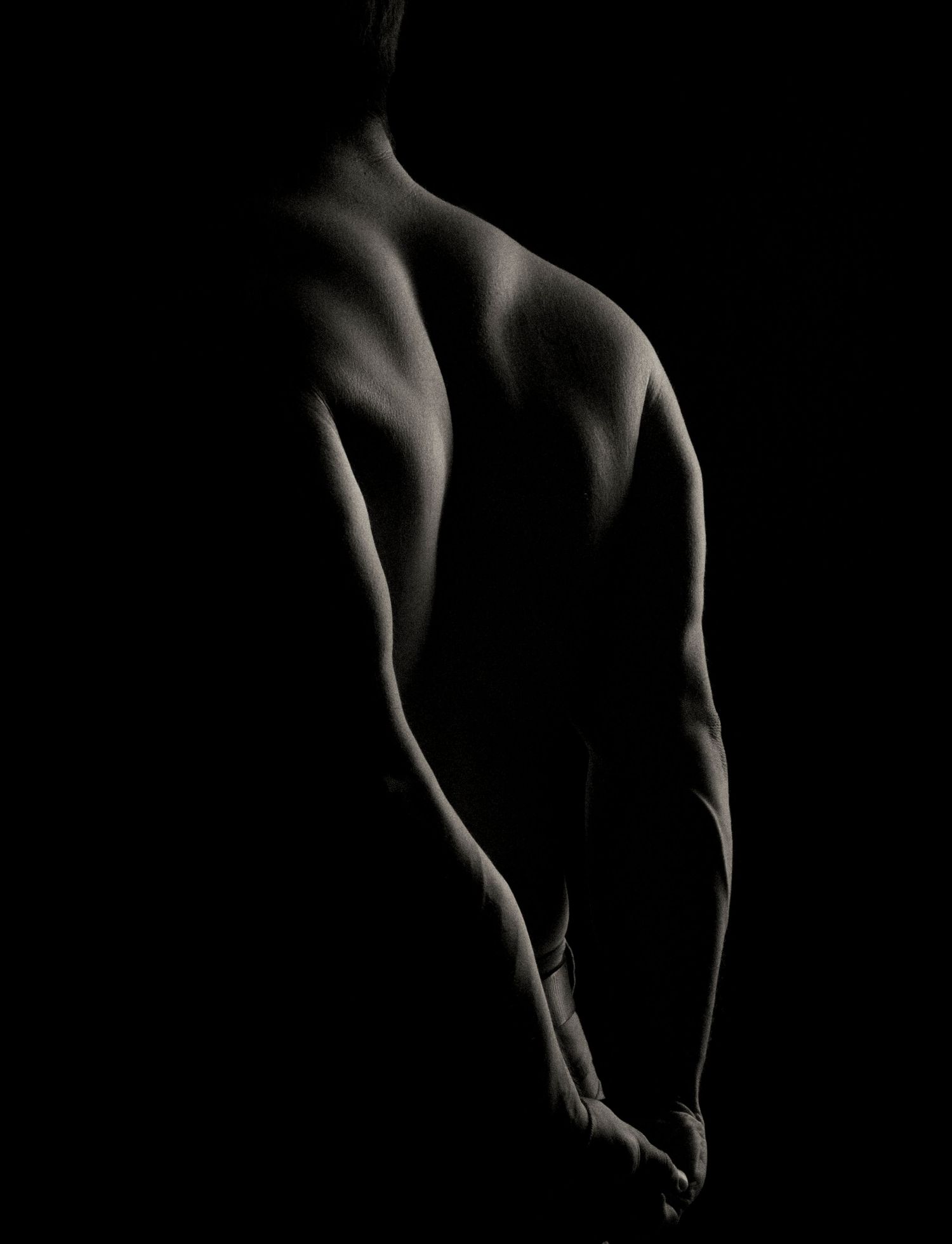 Dramatic black and white artistic photo of a muscular human back, highlighting defined shoulder and arm muscles.