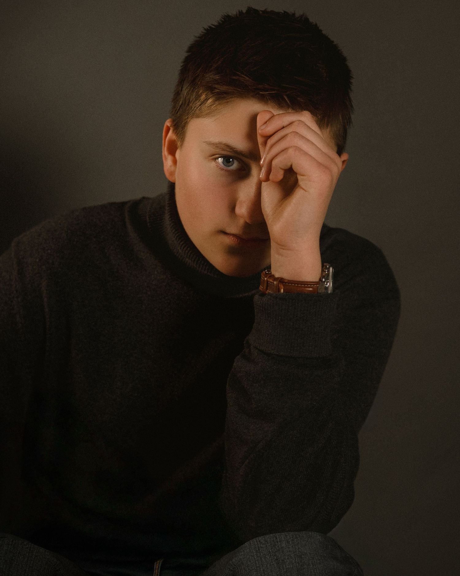 Dramatic portrait with dark tones and shadows against plain background.