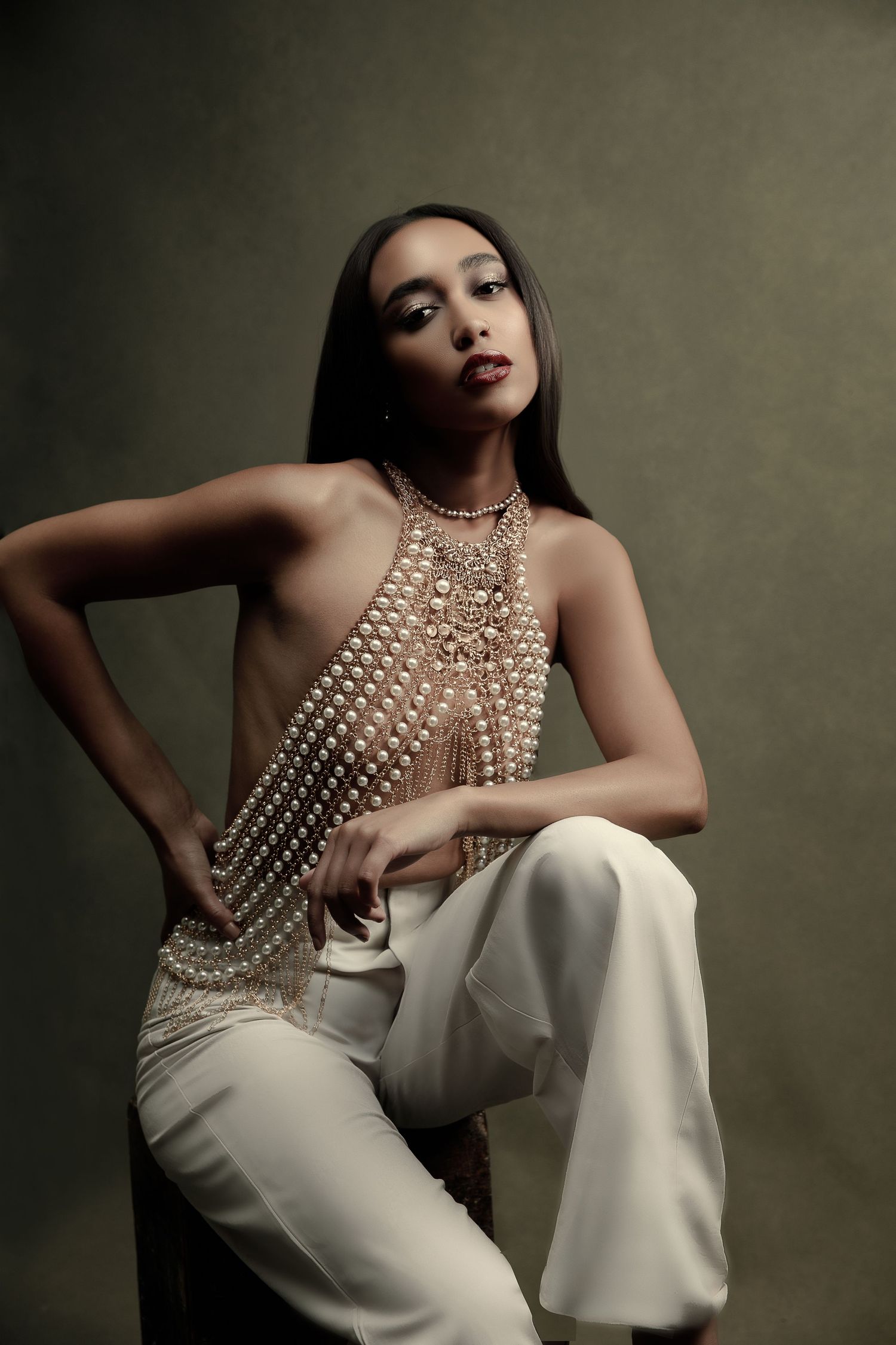 Fashion model in white pants and pearl embellished top poses elegantly against dark background.