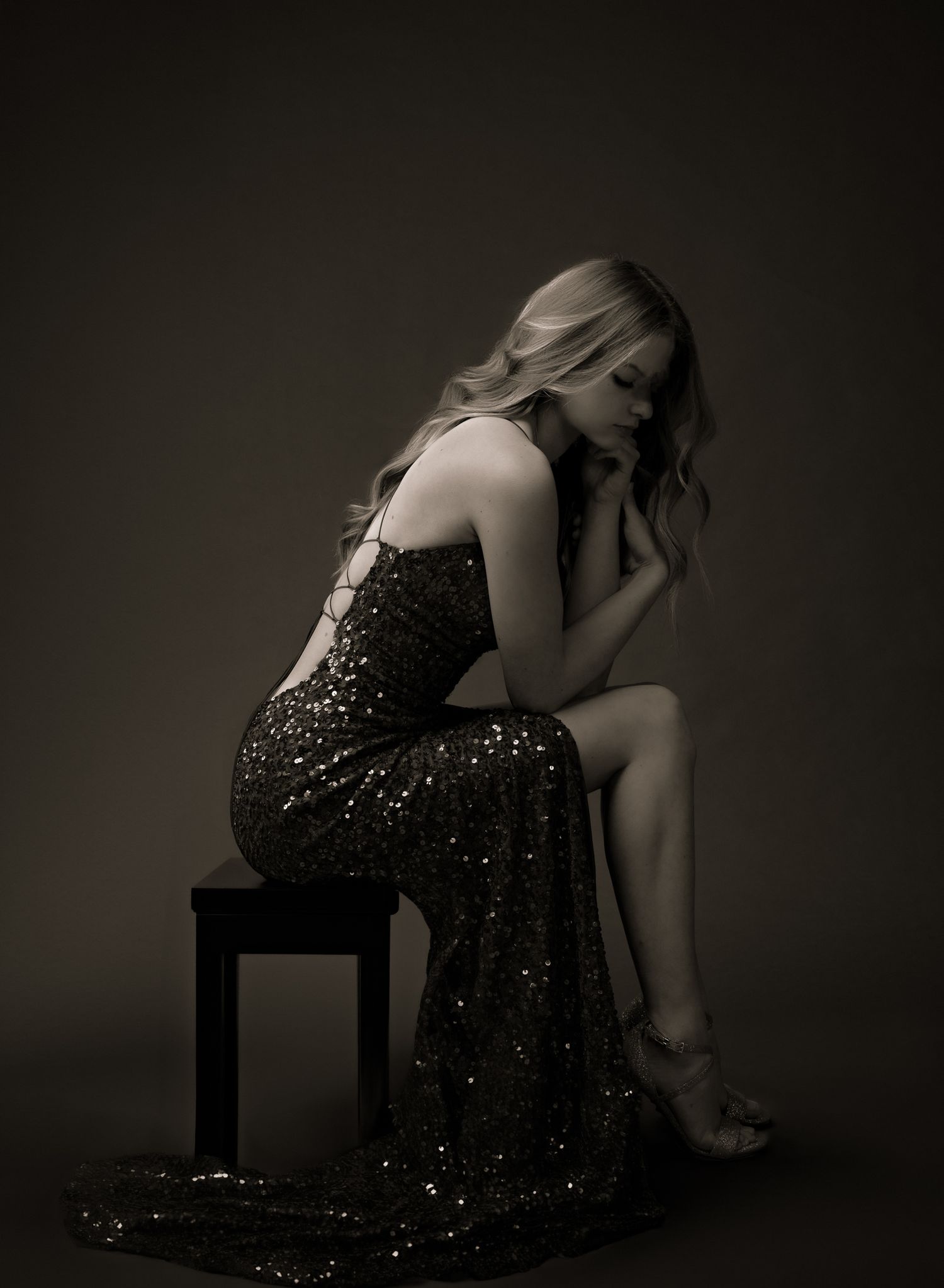 Dramatic black and white portrait in sequined evening gown on dark stool.