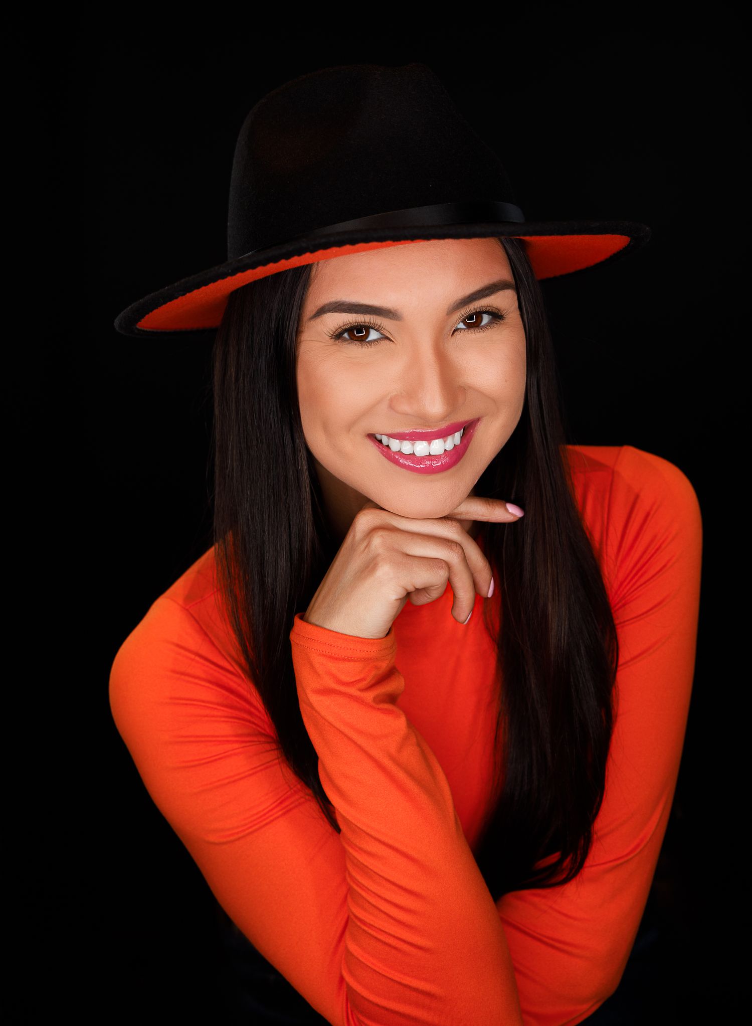 Vibrant portrait series with bright orange top and black hat against dark background.