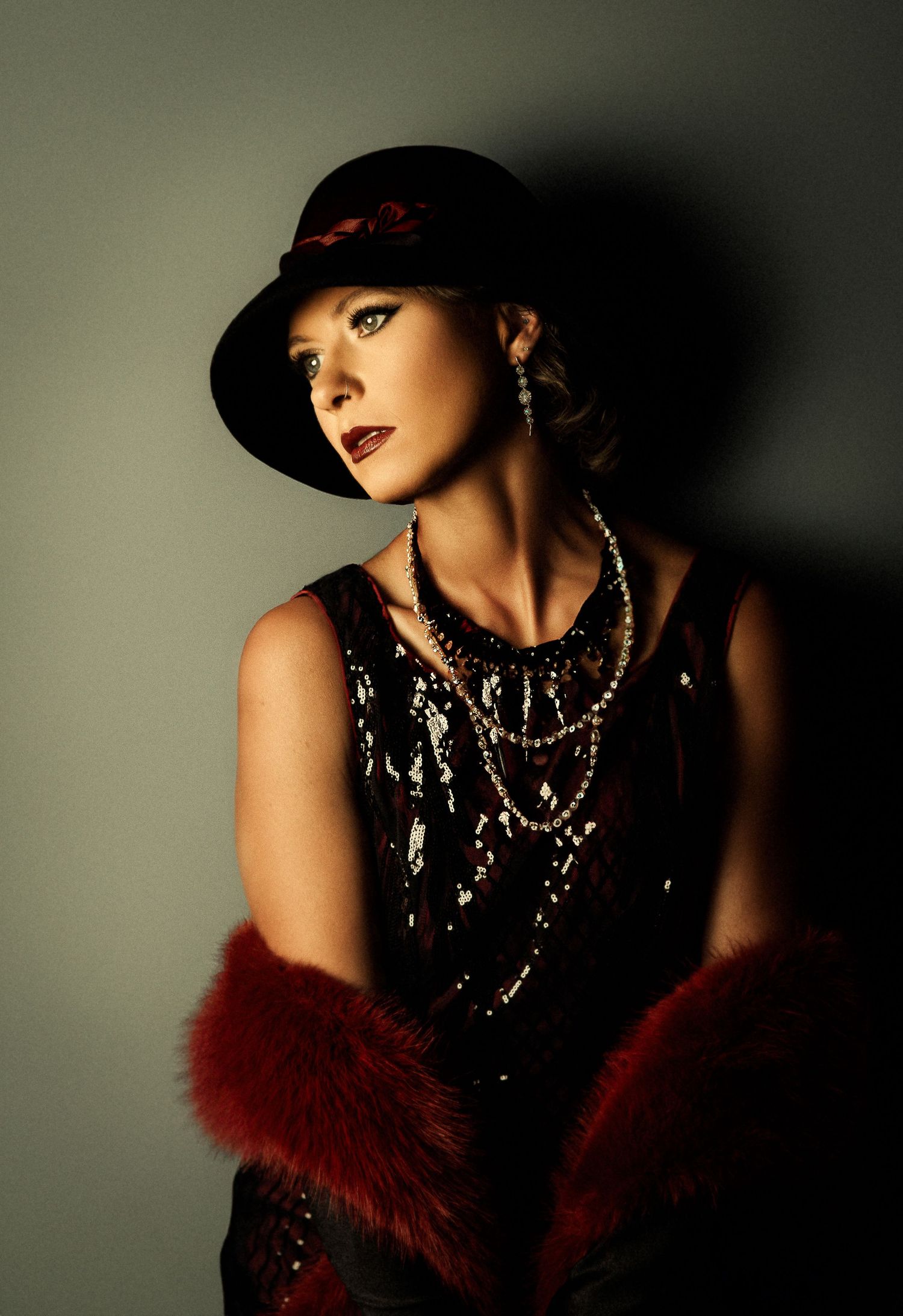Dramatic fashion portrait with red fur stole and sparkling statement necklace against dark background.