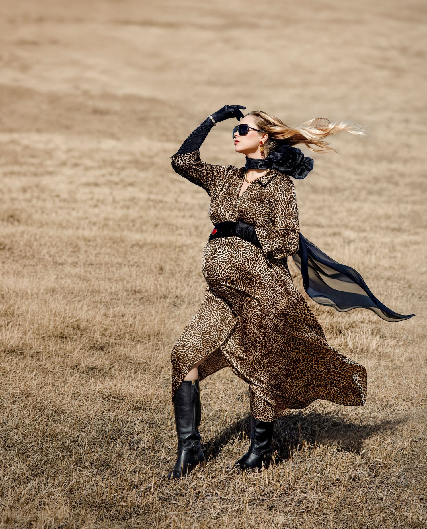 A figure in a flowing leopard print coat twirls dramatically in a field creating a sweeping motion effect.