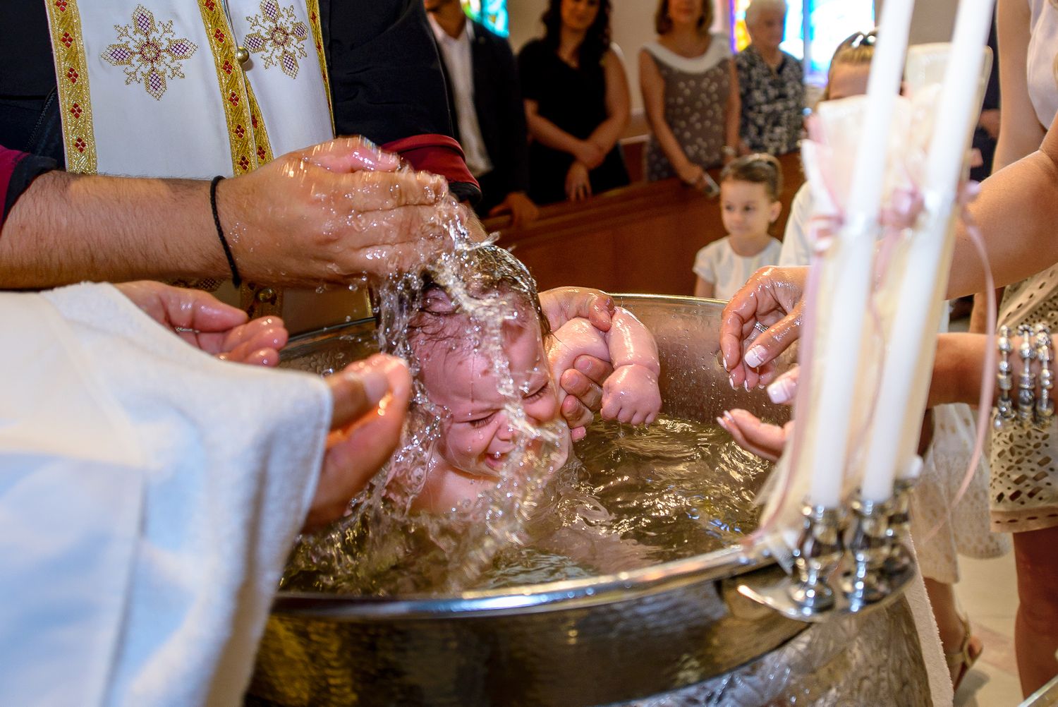 Close-up of infant being immersed in baptismal font during Orthodox Christian christening ceremony.