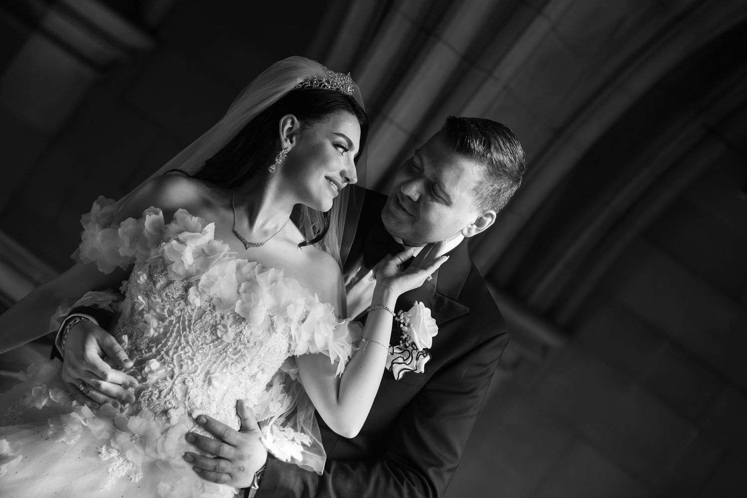 Bride and groom share intimate moment in black and white photo beneath grand stone columns.