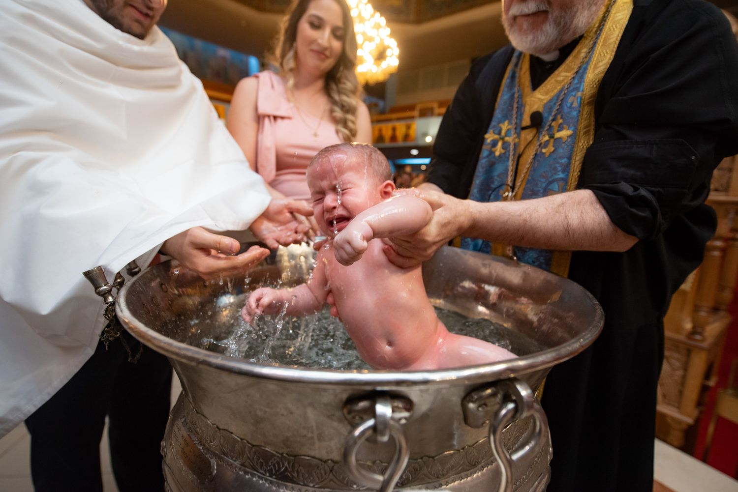 Baby being baptized in ornate silver font by  a priest during Orthodox Christian baptism ceremony at St Demetrios Orthodox Church in Toronto