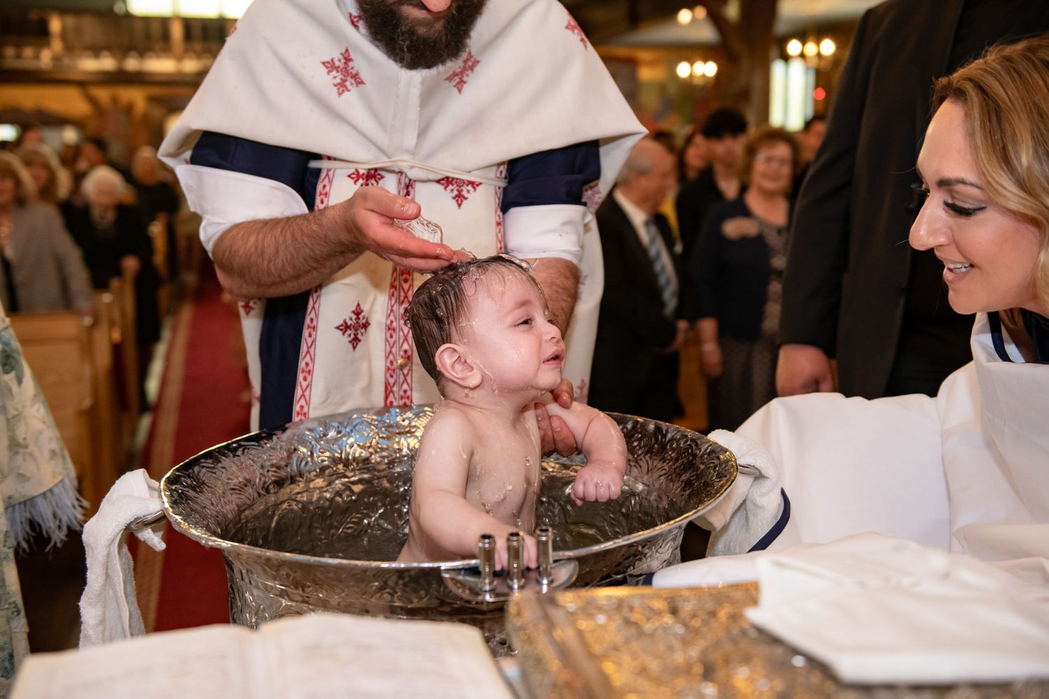 Baby being baptized during a Greek Orthodox baptism ceremony in Toronto as holy water is poured over the child.