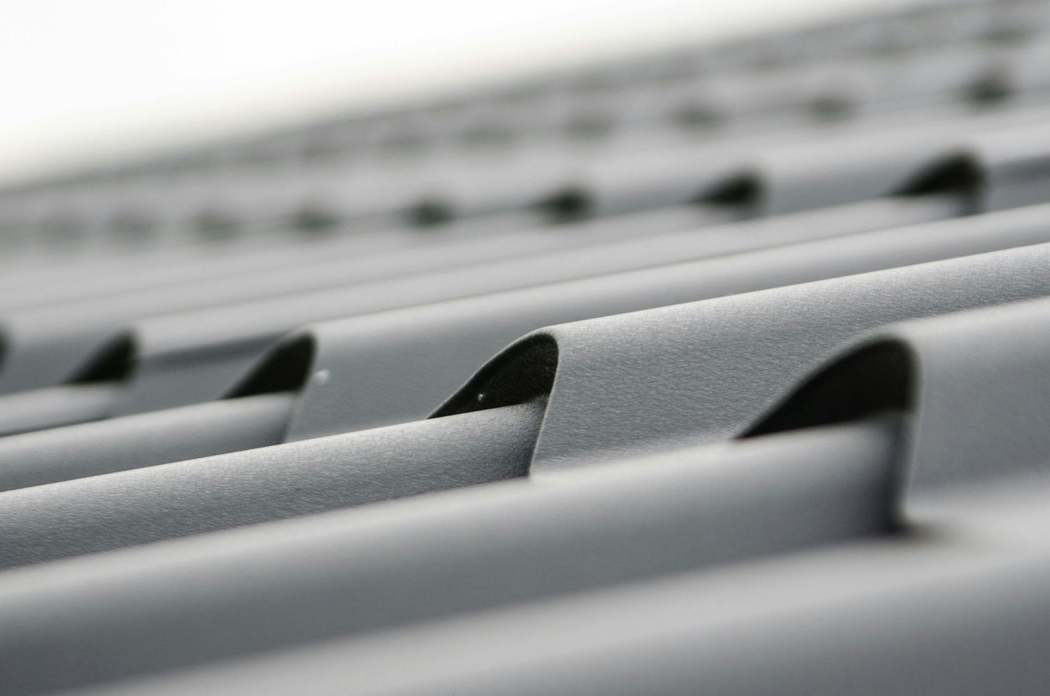 A close-up view of gray metal roofing panels with parallel lines creating a repeating geometric pattern.