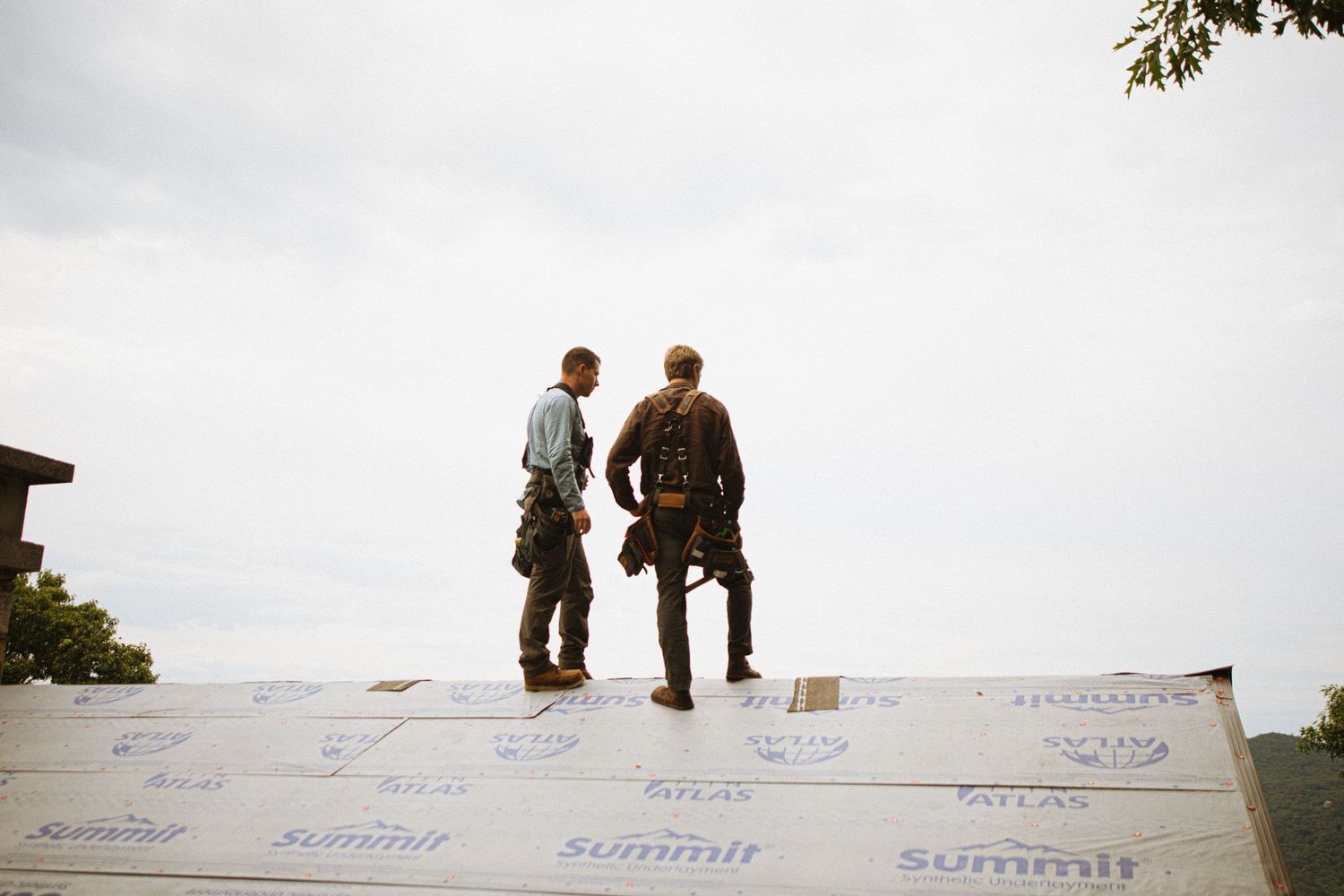 Two roofers standing on a roof covered with Summit underlayment, wearing safety harnesses against an overcast sky.