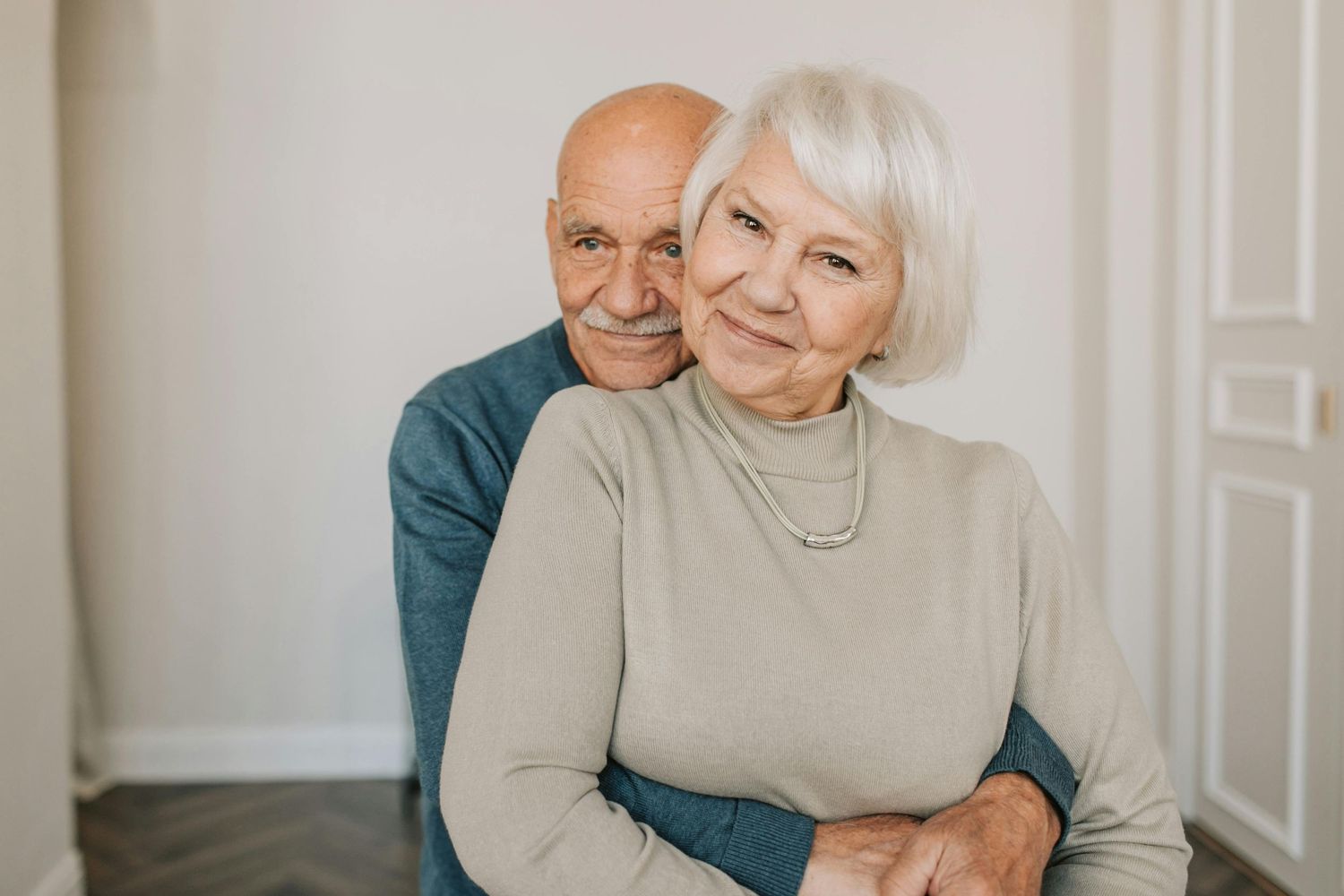 Loving senior couple sharing affectionate moments against white wall.