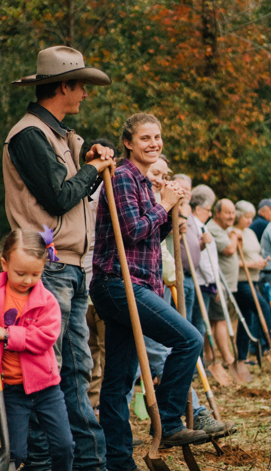 Group of people holding garden tools outdoors during a community planting event in autumn.