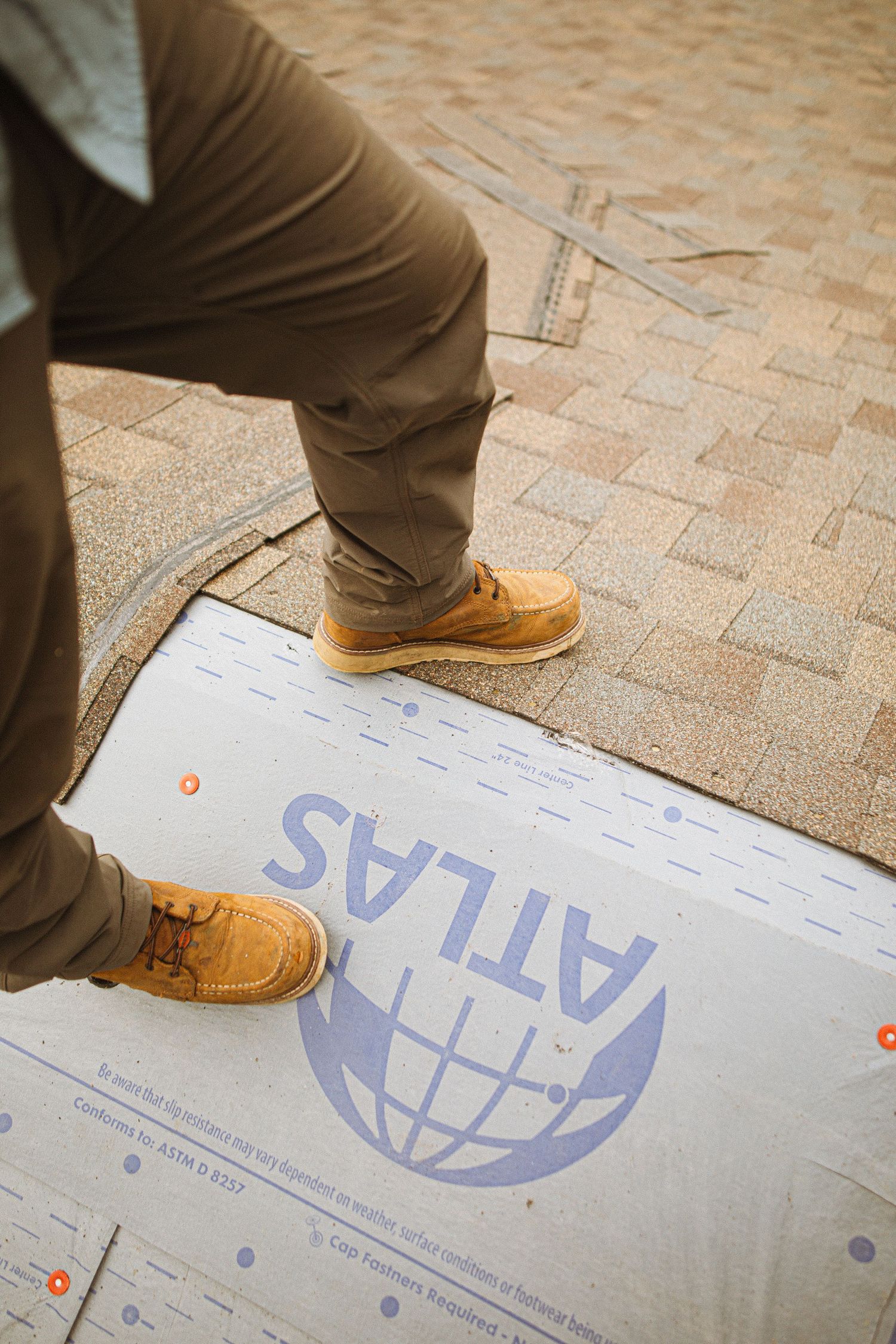 Roofer standing on Atlas underlayment during shingle roof installation, wearing tan work boots and khaki pants.