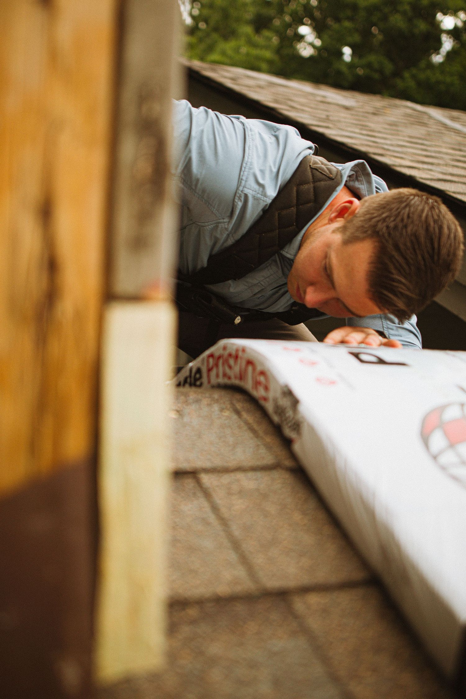 A roofer inspects shingles up close while leaning over a Pristine roofing material during a residential roof installation.