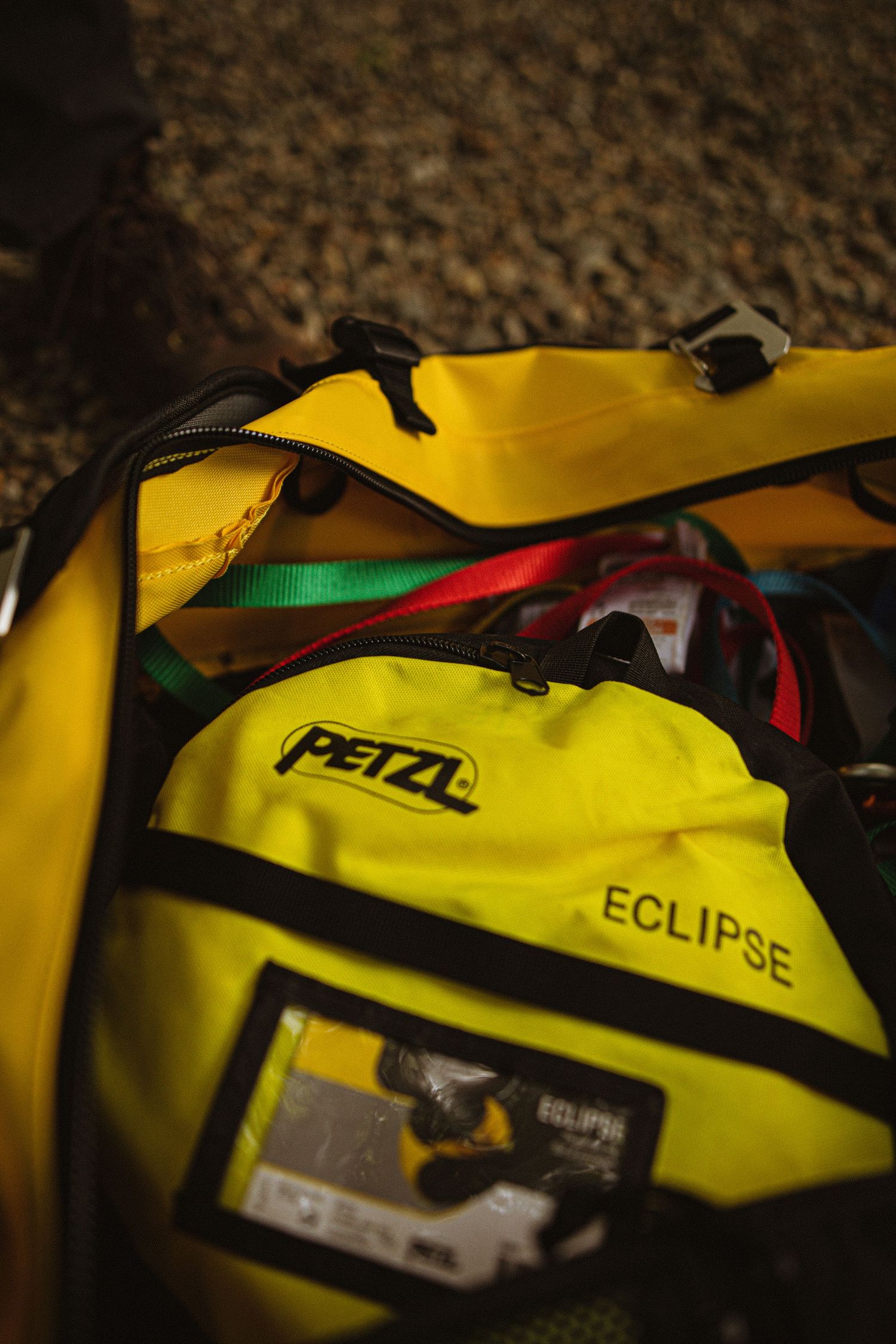 Yellow Petzl Eclipse backpack filled with colorful climbing gear and equipment, photographed outdoors on rocky ground.
