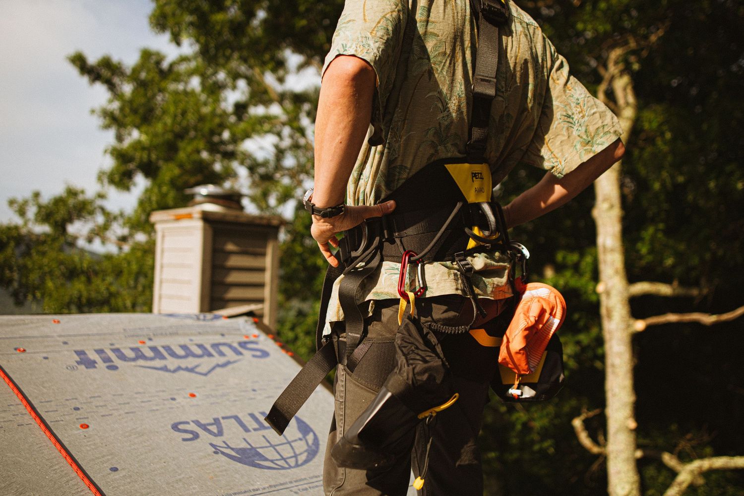 Roofer wearing safety harness and tool belt working on a roof with Atlas Summit underlayment on a sunny day.