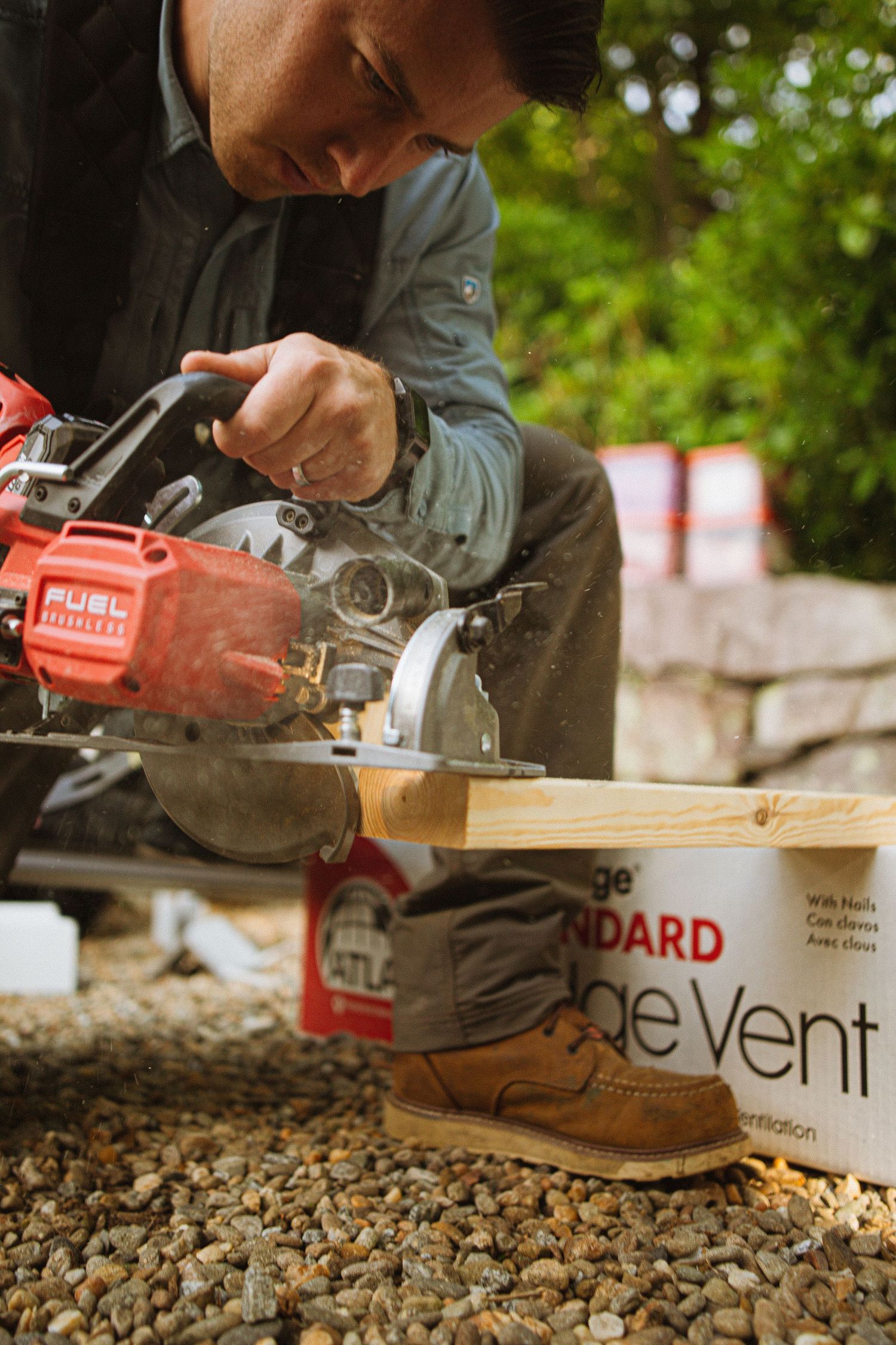 A contractor uses a Milwaukee Fuel circular saw to cut lumber on a construction site with ridge vent packaging nearby.