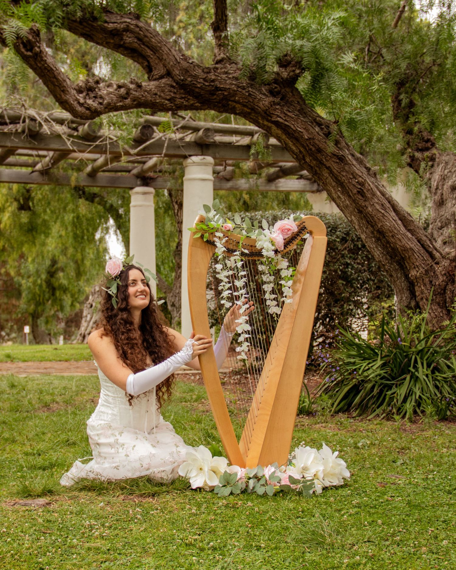 Woman playing harp beneath a tree decorated with flowers | Nuvue Visuals creative portrait photography in San Diego Presidio Park