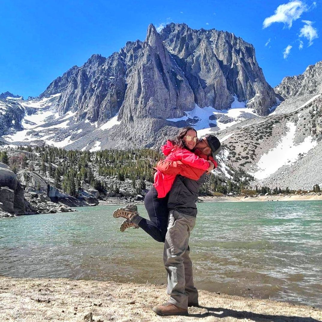 Couple embracing by an alpine lake with snow-capped mountains | Nuvue Visuals adventure photography in California