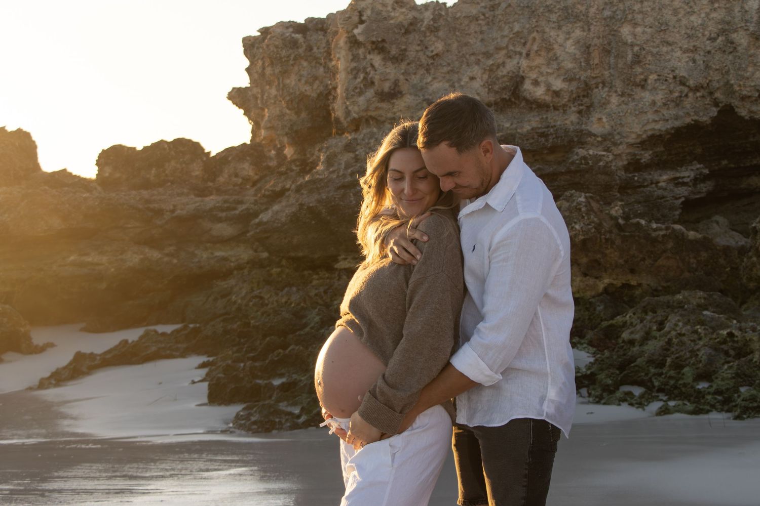 Expecting mum holding her baby bump while smiling at her partner during a relaxed outdoor maternity session in Perth.