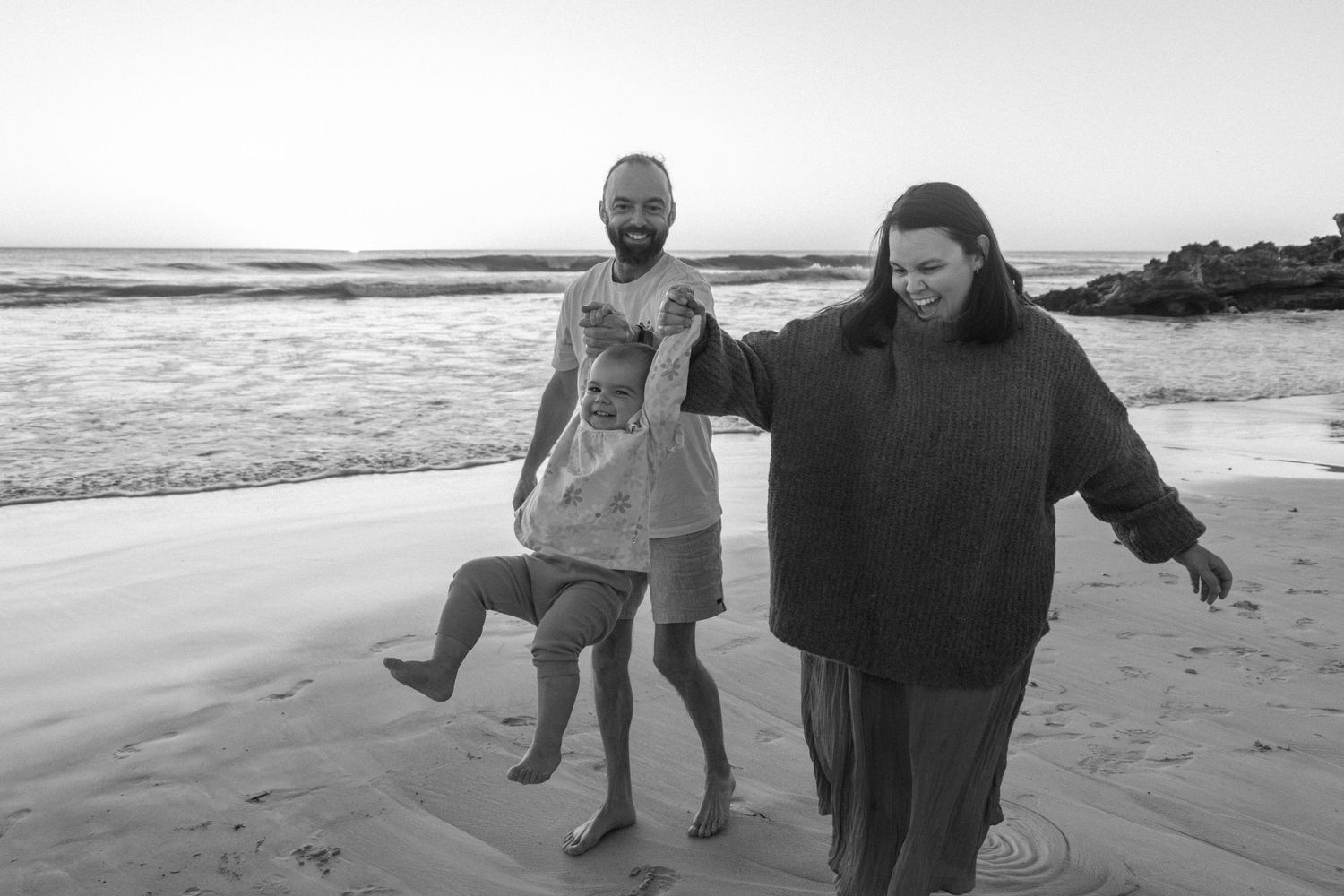 Candid family photos at Mullaloo Beach with parents swinging toddler, natural laughter at sunset.