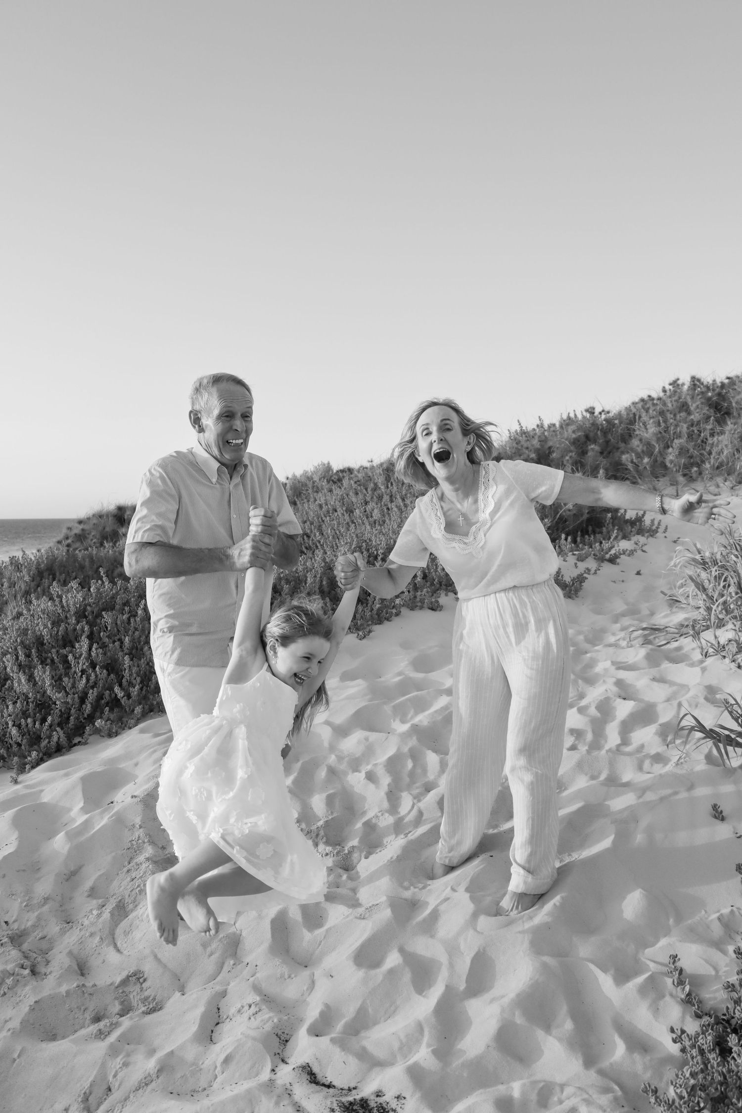 Grandparents swinging their granddaughter at the beach during a family photography session in Perth.